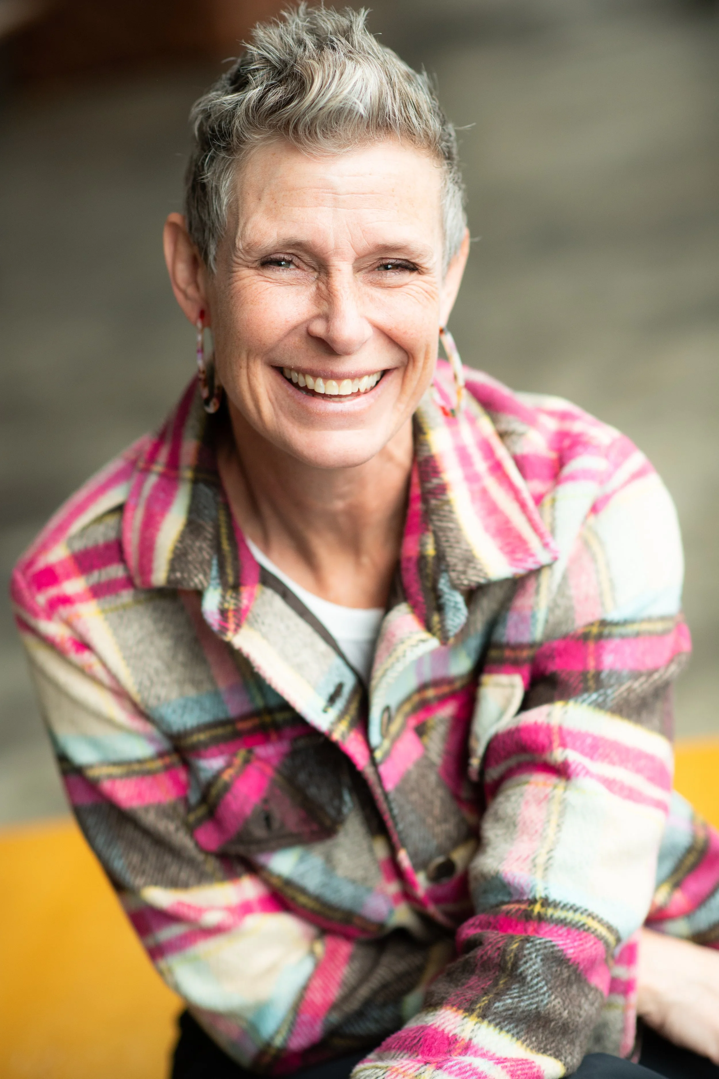 A white women smiling with short gray hair and pink flannel 