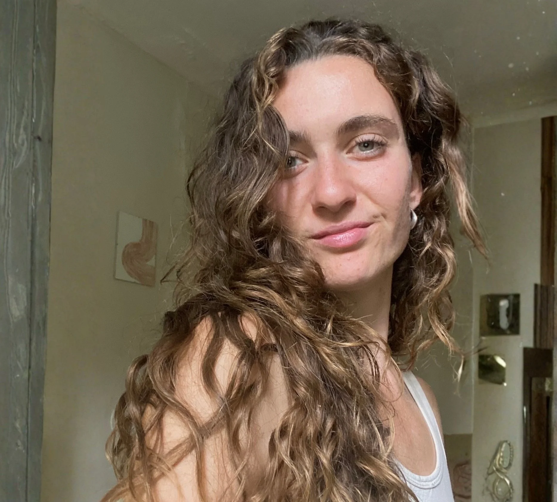 A woman smiling in a green greenhouse, surrounded by large lush plants.