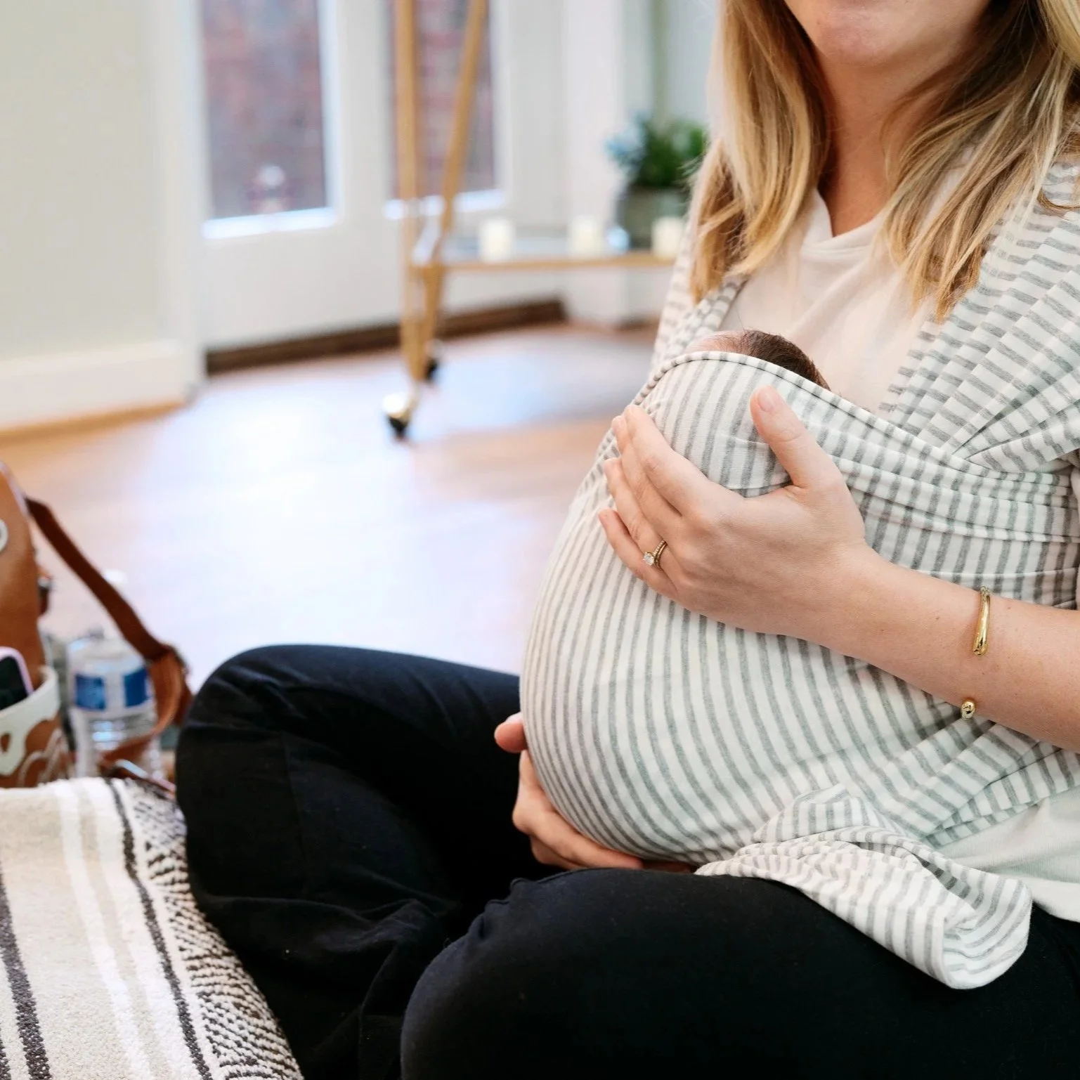 Two women sitting on a wooden bench, each holding a baby, smiling and laughing in front of a plain white wall.