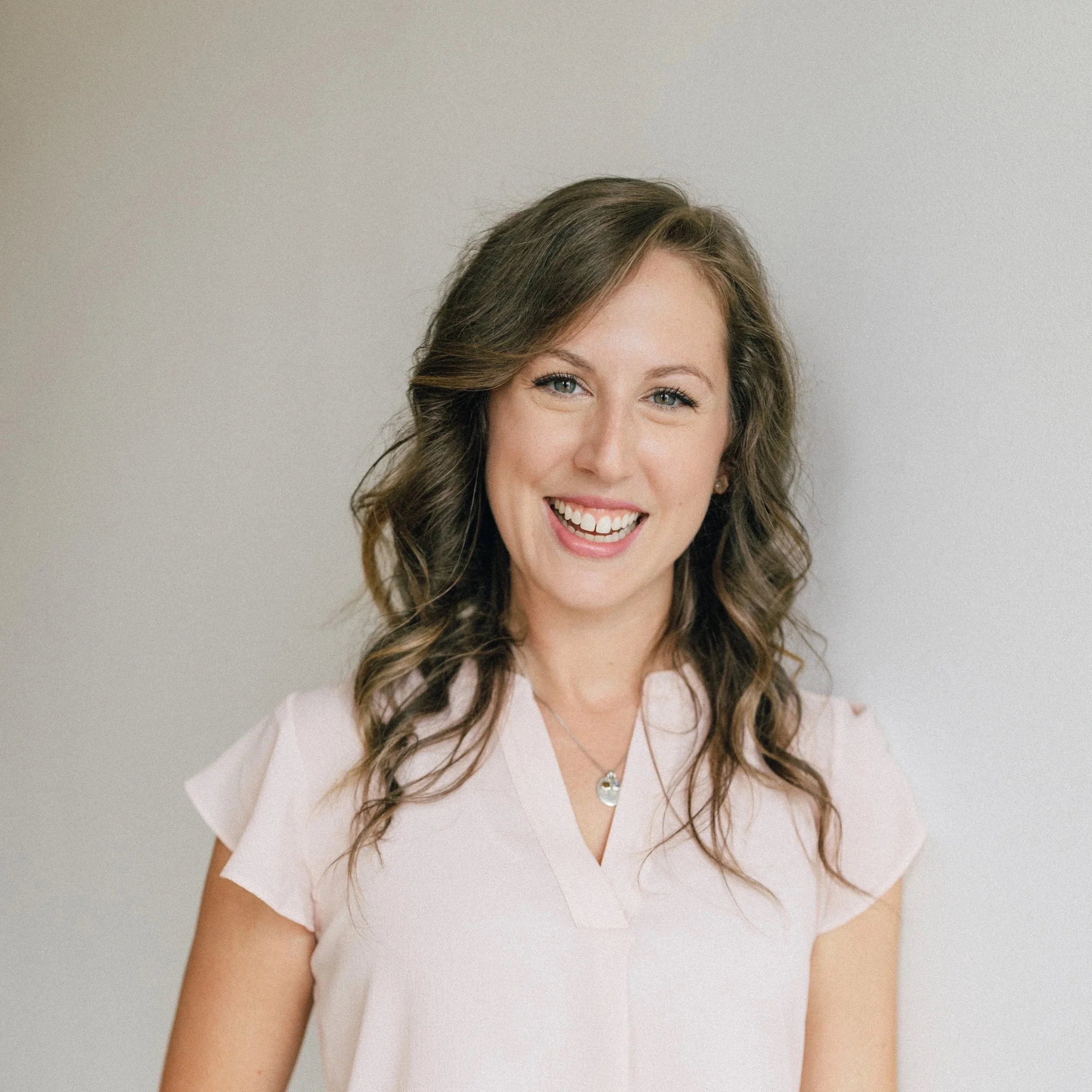 A man with curly dark hair, glasses, and a beard, wearing a dark sweater, looking slightly to his right in a well-lit room with a blurred plant in the background.