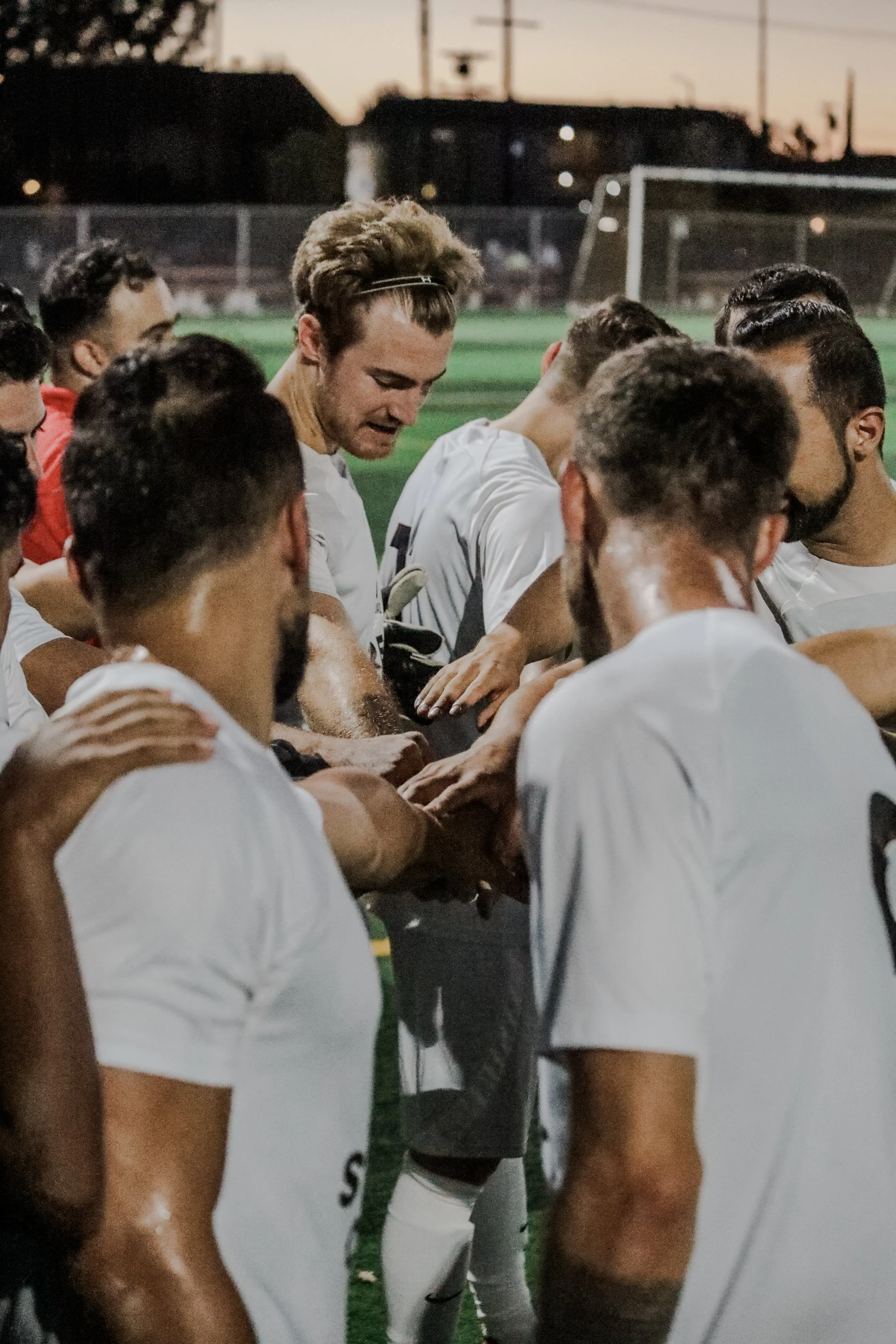 A group of soccer players huddle together on a field during sunset, engaging in a team prayer or pep talk.