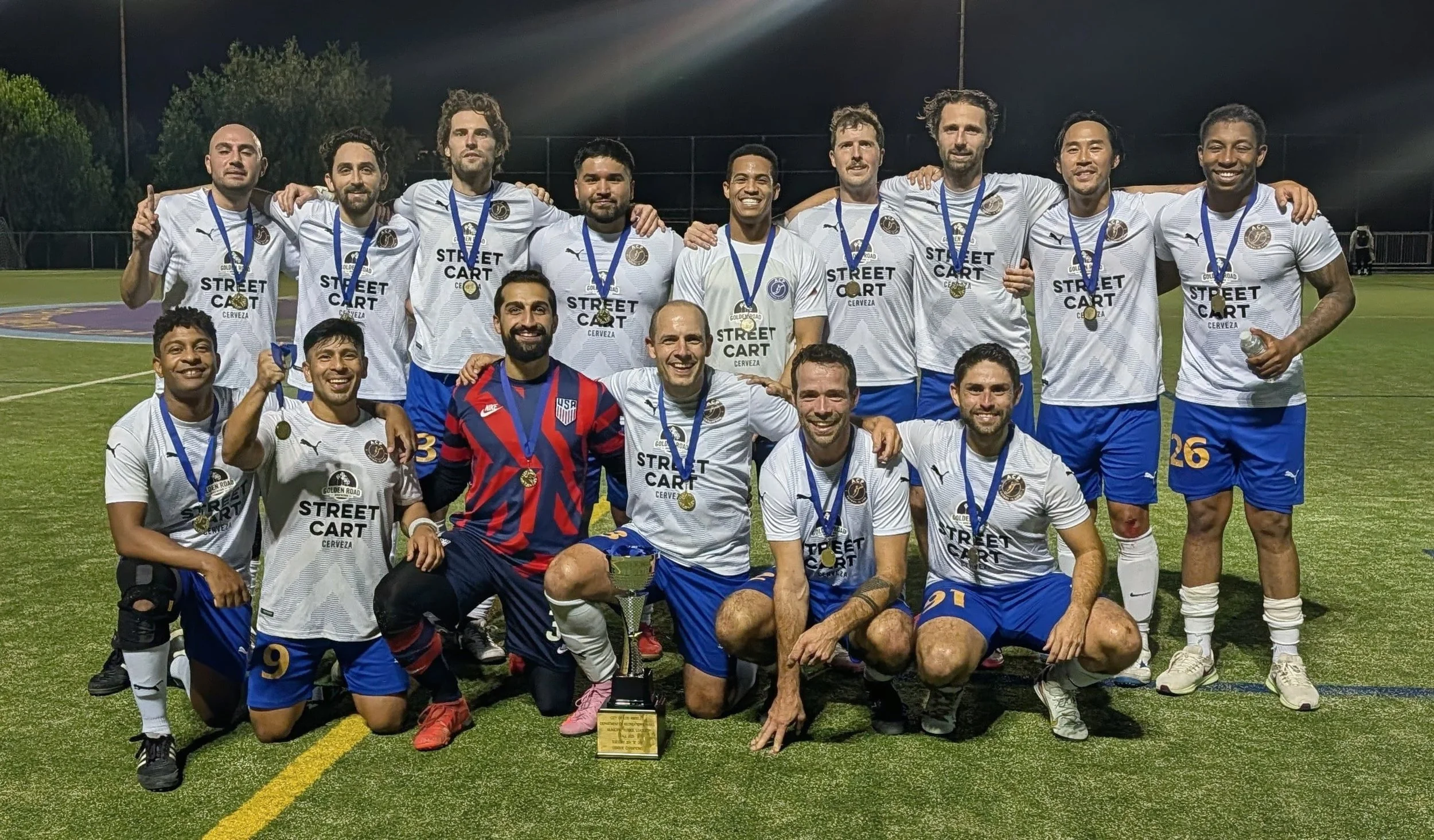 A circular logo with a navy blue background and gold border that reads 'ACF FUTBOL IS LIFE' at the bottom. The center features a stylized gold letter 'F' intertwined with a fish, with 'EST 1987' written on either side of the fish.