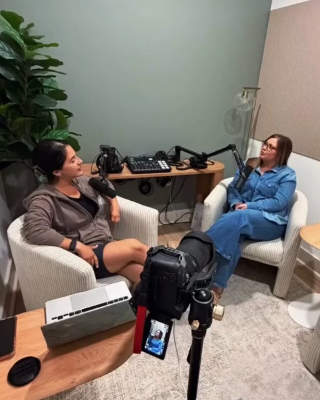 Two business woman setup for podcasting, featuring two microphones, audio equipment, laptop, and video camera for production