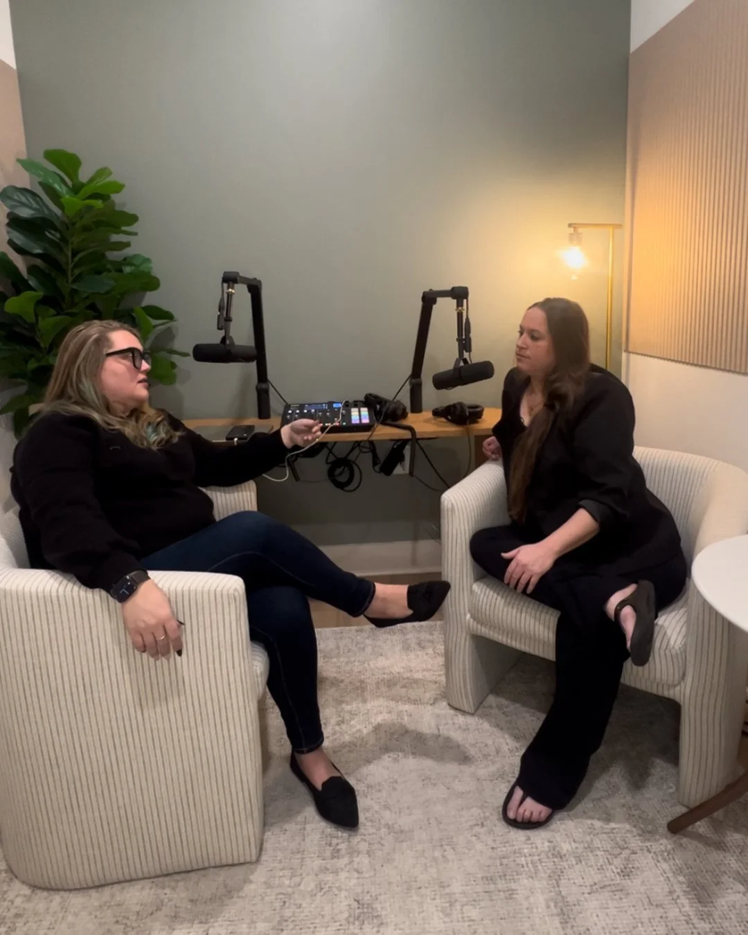 Two women in business suits chatting for a podcast episode