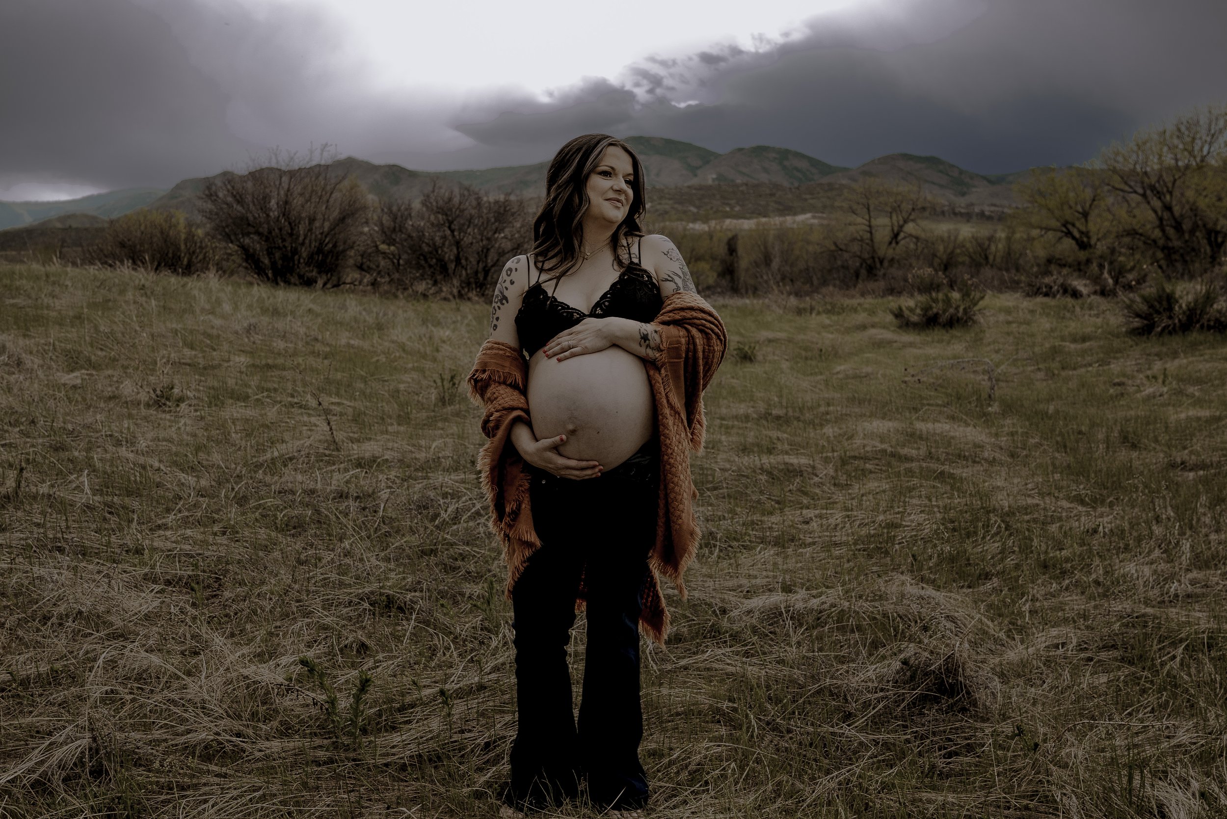Momma to be holding her baby bump with dramatic clouds behind her