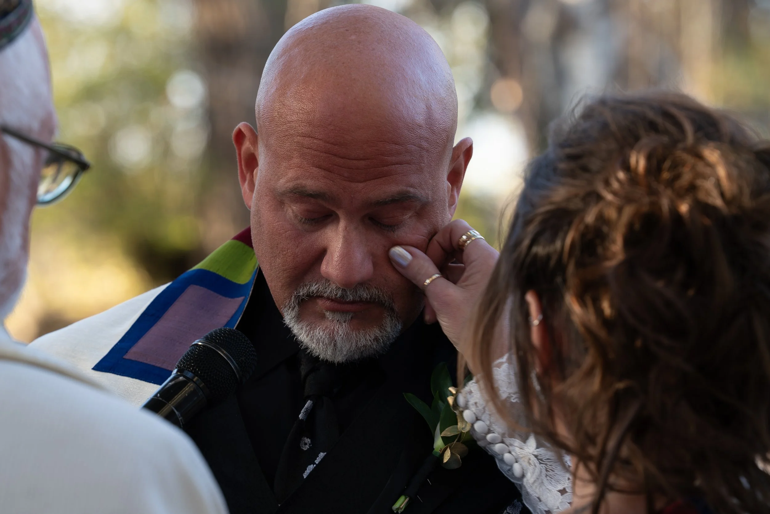 Emotional wedding ceremony moment as a bride gently wipes a tear from the groom’s face during their vows, photographed by a Colorado wedding photographer