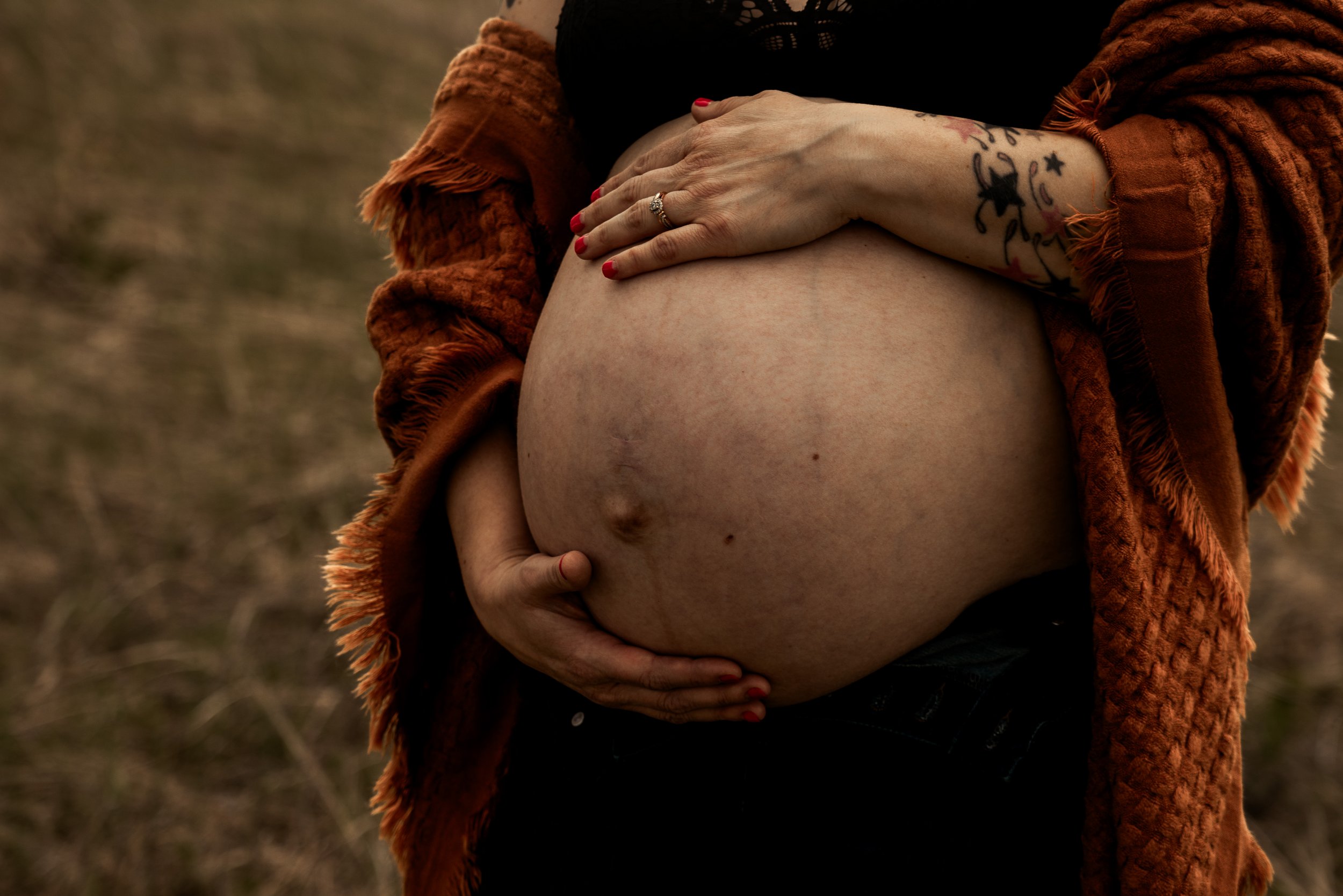 Close up of a pregnant belly with mother's hands craddling on the top and bottom of the growing belly.