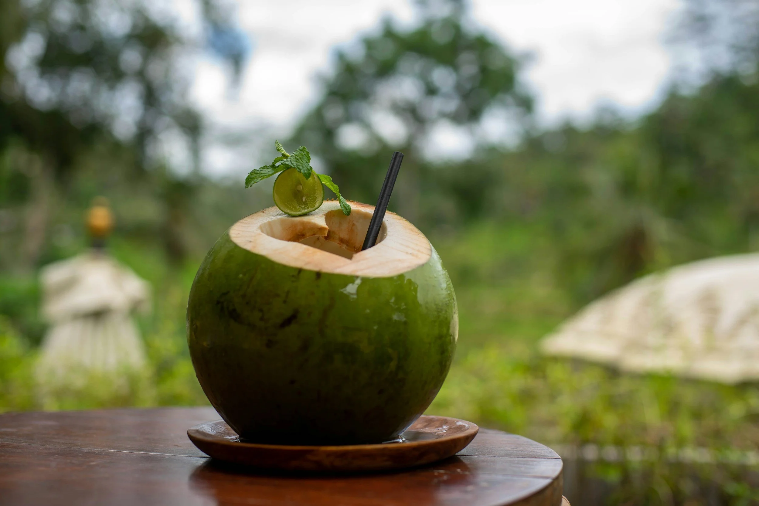 Coconut drink with a black straw placed on a wooden table outdoors.