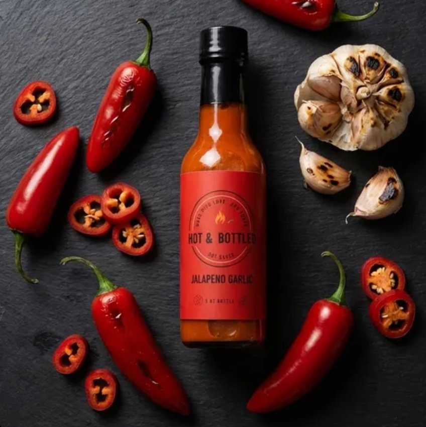 Red label with the text 'Hot & Bottled' and 'Jalapeno Garlic.' A chili pepper with flames above it, and words 'Made with love...and smoke,' and 'Hot sauce' encircling the chili.