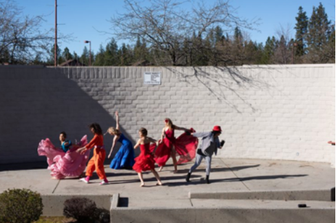 A group of brightly dressed people dance outdoors on a sunny day.