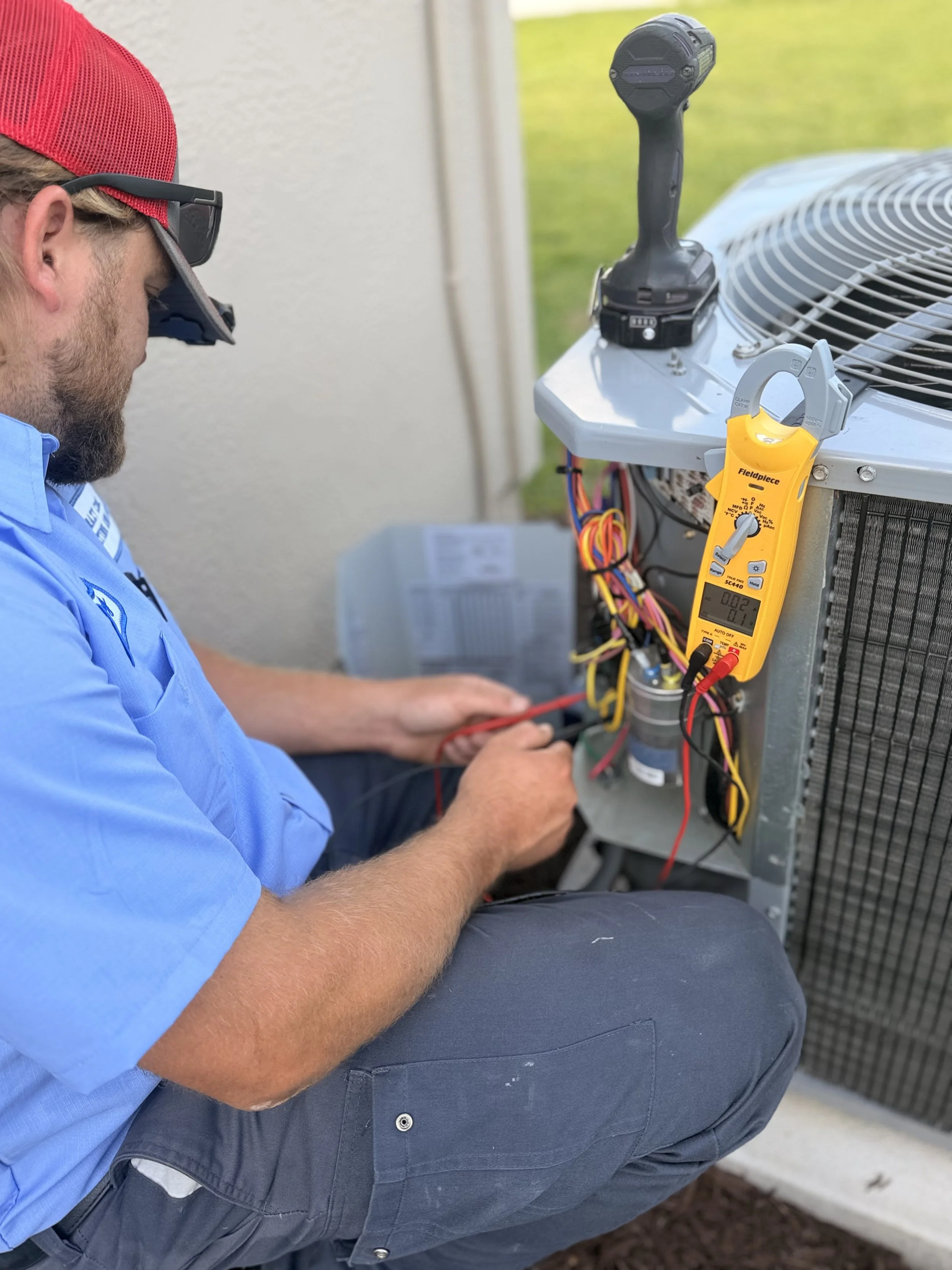 Technician working on an air conditioning unit, using a multimeter and a screwdriver, outdoors.