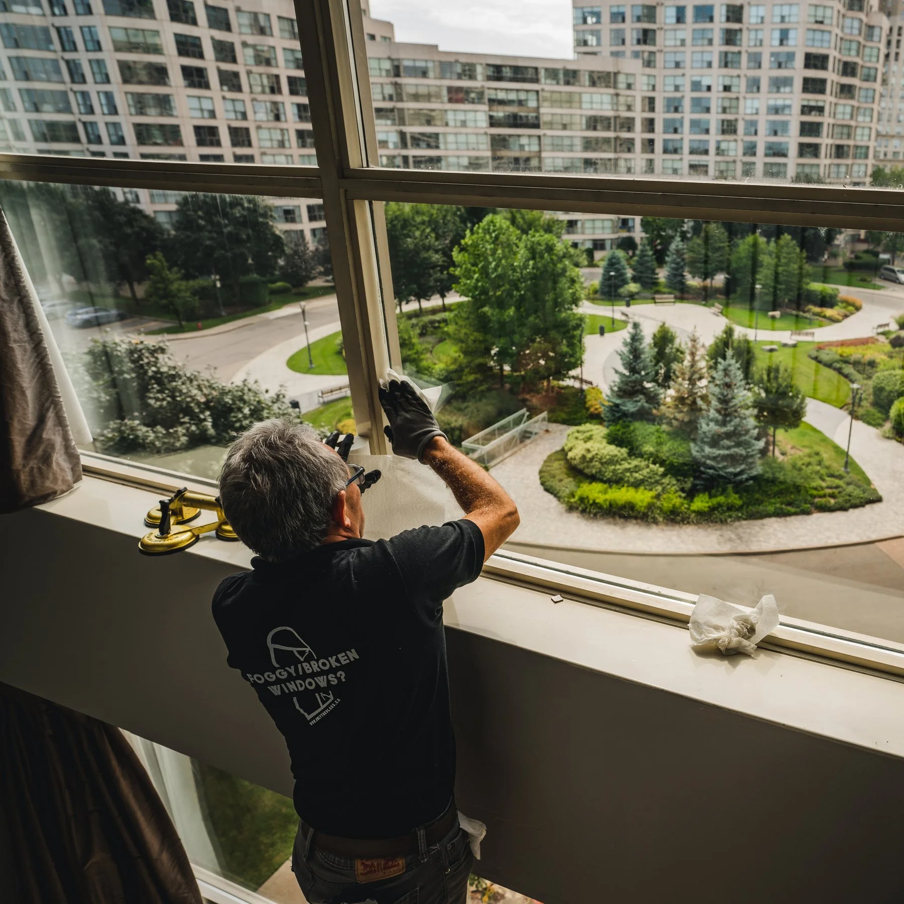 A WRE technician servicing a window inside an occupied condominium unit overlooking the building grounds