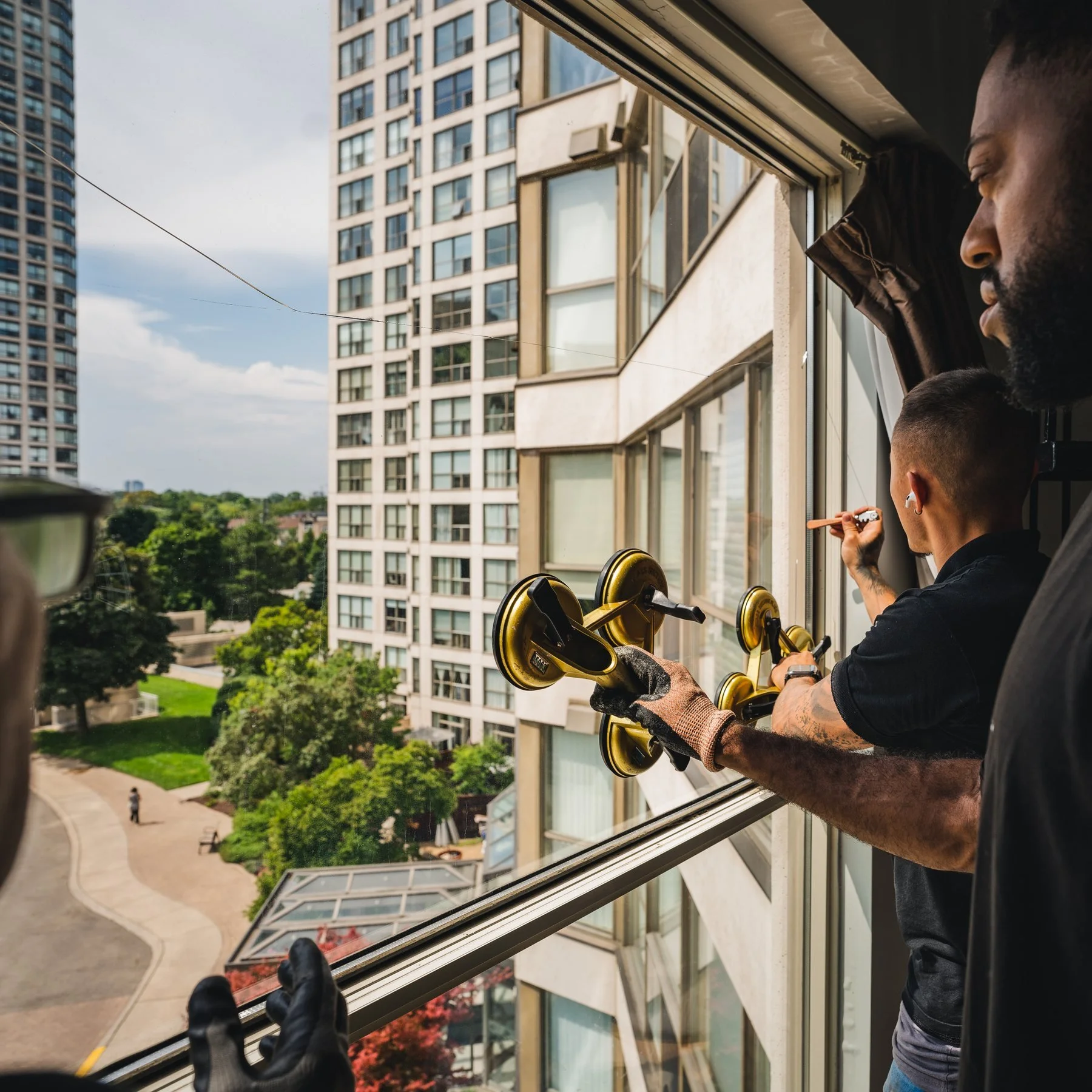WRE technicians lifting a sealed glass unit into a high-rise condominium window with glass suction cups