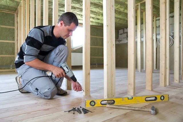 Man installing hardwood flooring inside a framed room under construction.