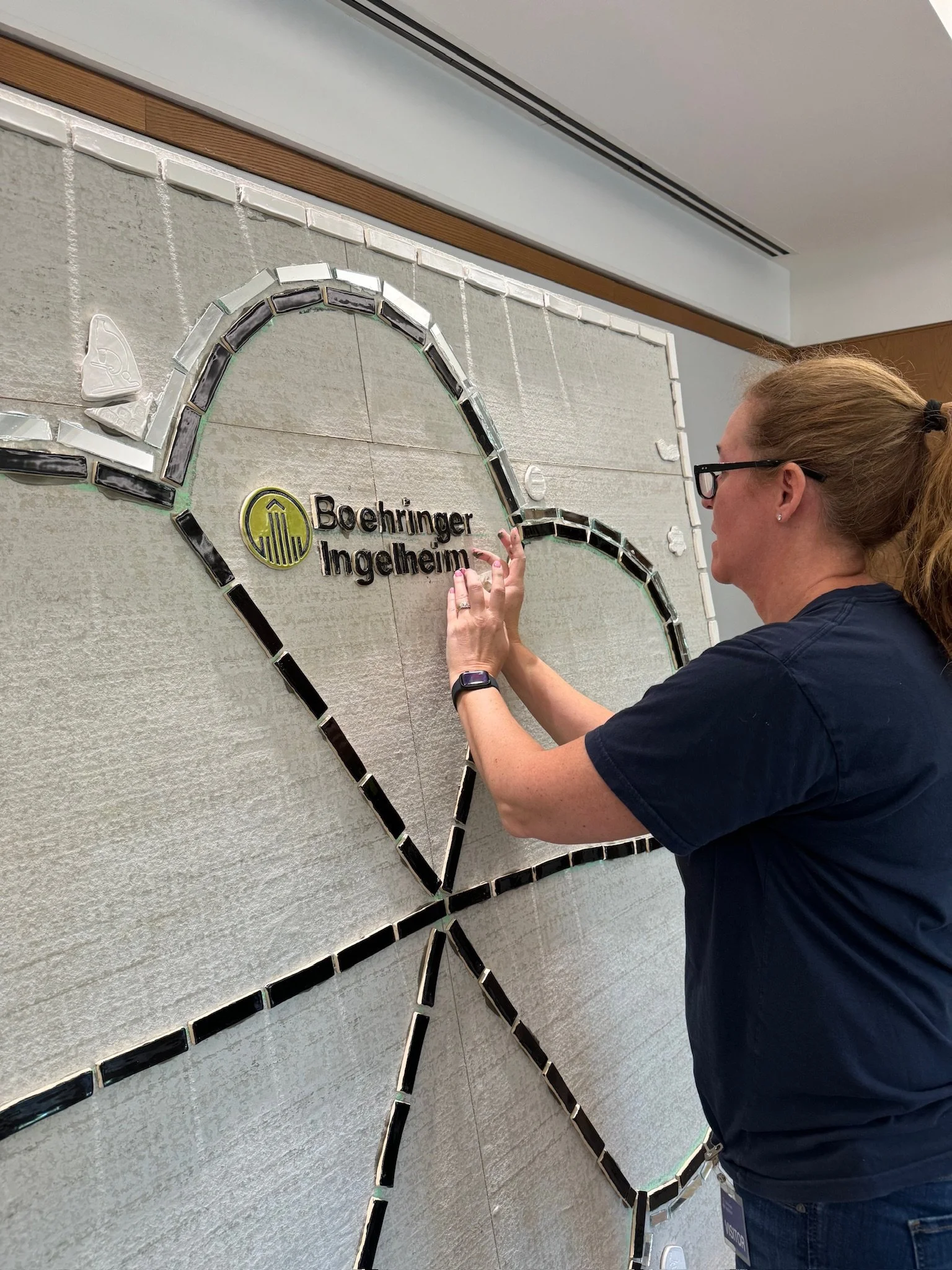 Woman installing a sign on a wall that reads 'Boehringer Ingelheim' inside a glass heart outline.