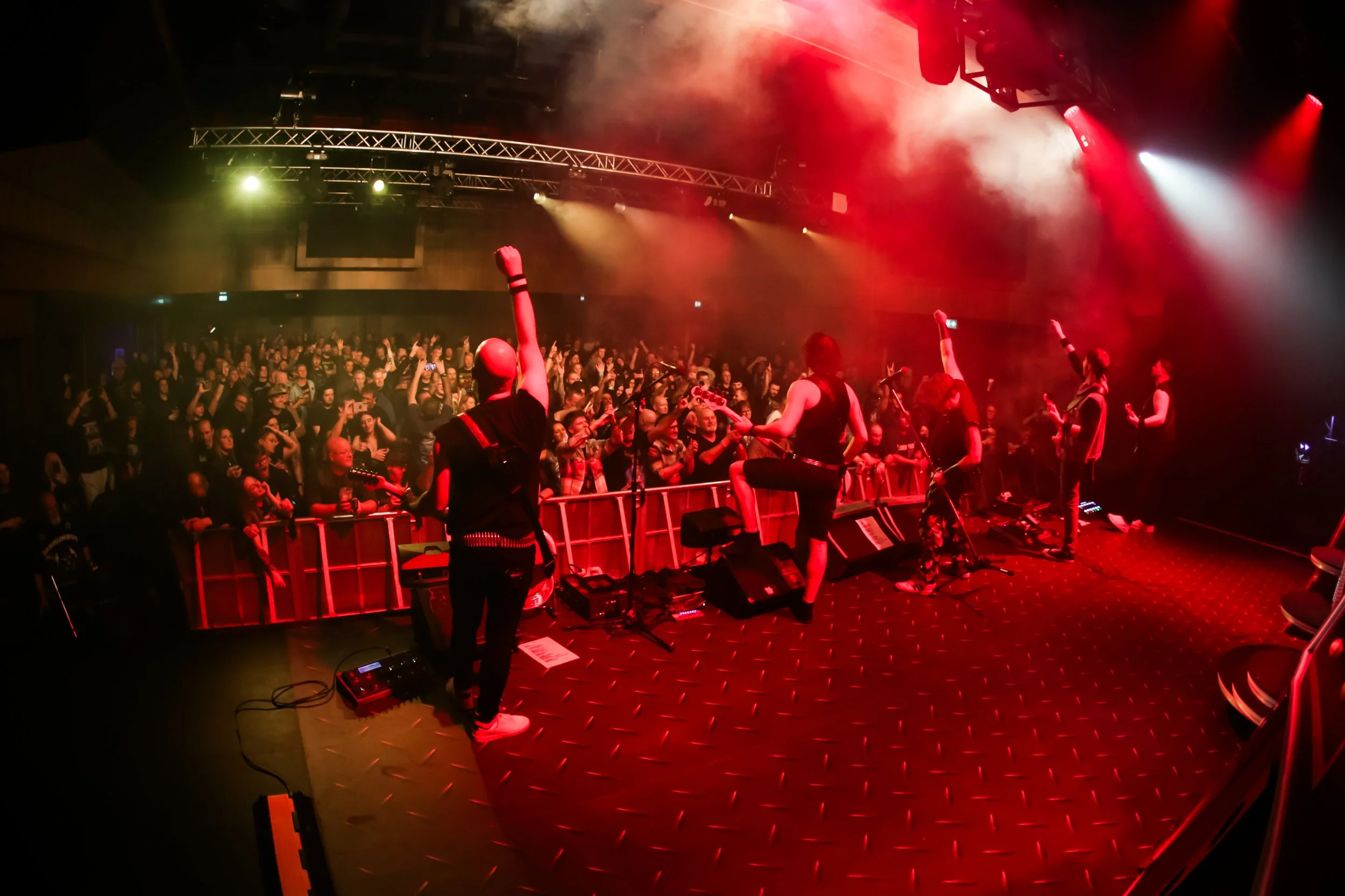 Band performing on stage during concert with audience cheering, colorful stage lights, and smoke effects.