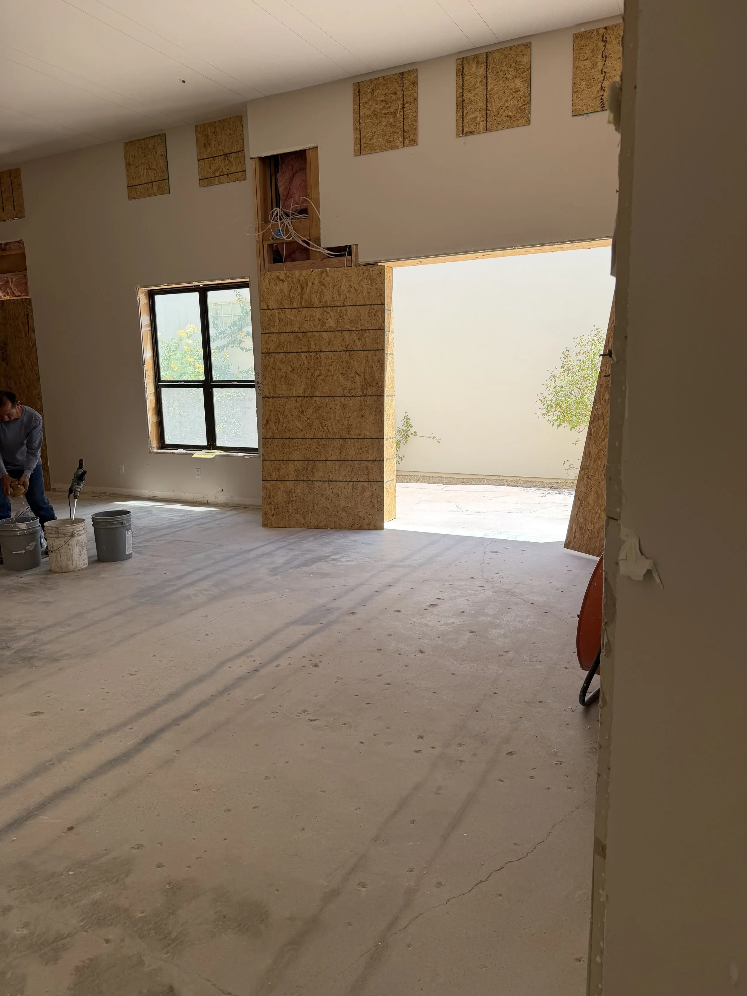 Interior of a house under construction with drywall and insulation, a window, and construction worker with buckets on the floor.