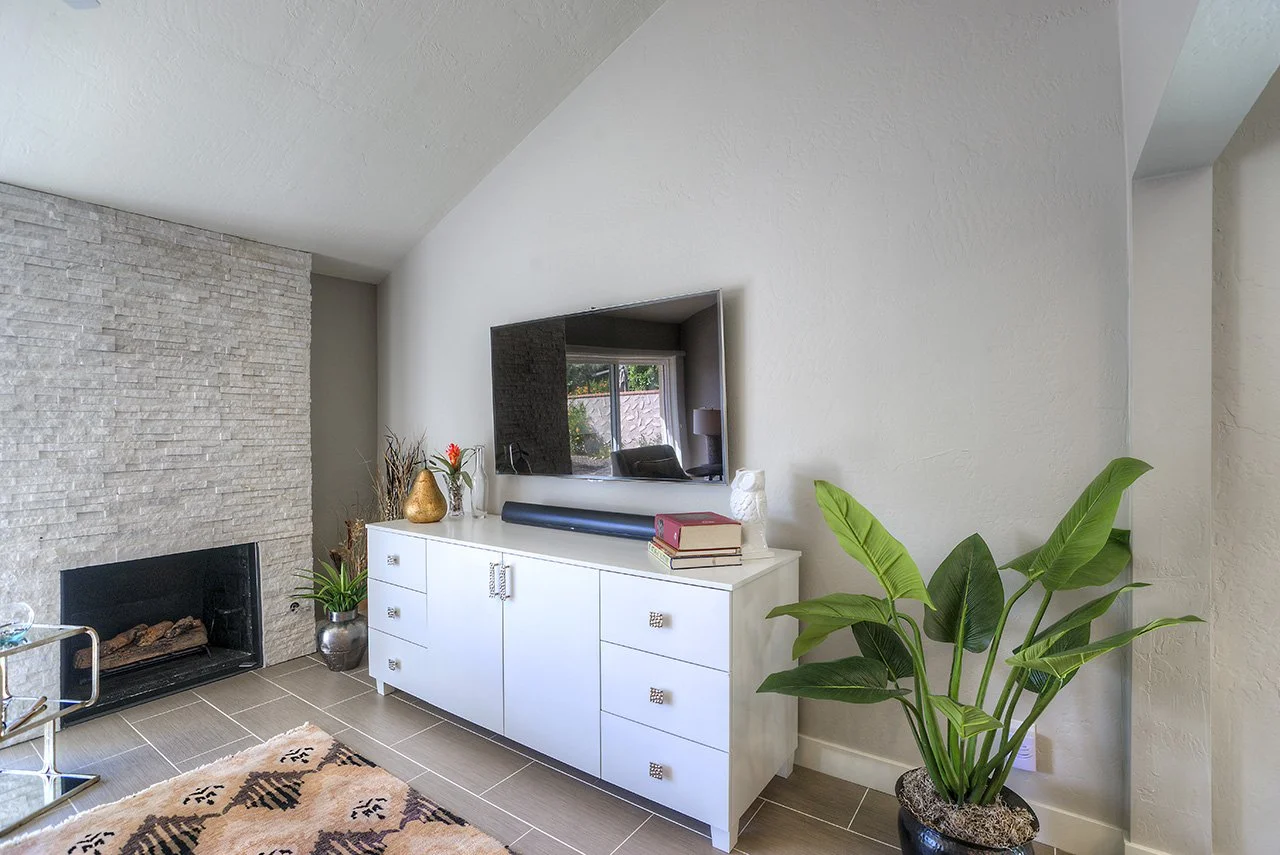 Living room with a white cabinet, a large flat-screen TV, decorative vases, a potted plant, and a fireplace, with a rug on the floor.
