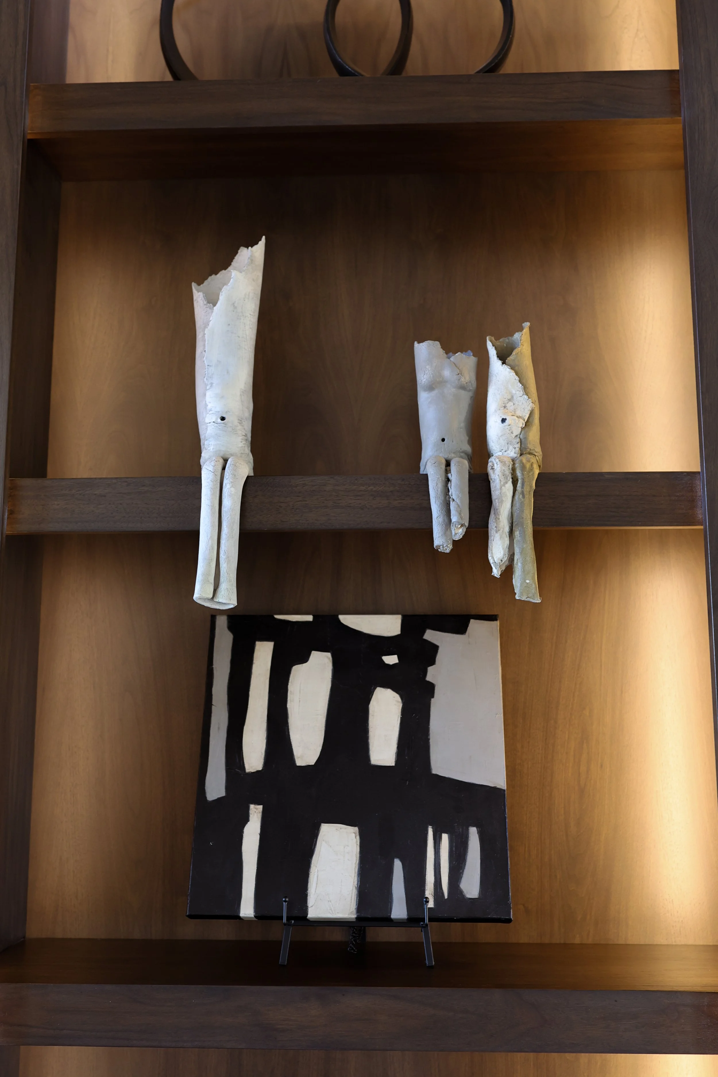 A wooden shelf holding three animal skulls with antlers and a black and white abstract painting with bold, blocky shapes.