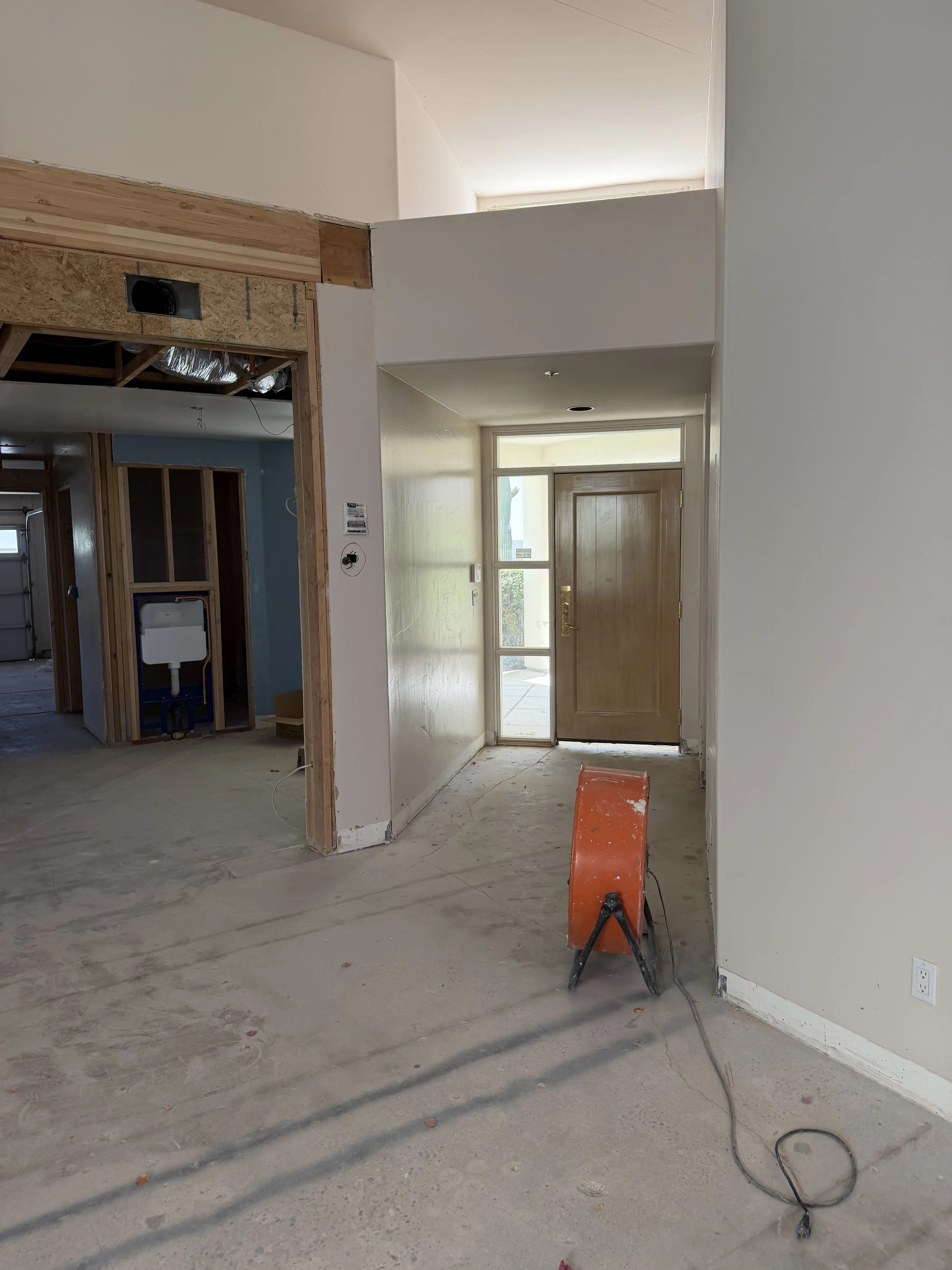 Interior of a house under construction with open walls, a front door, and construction tools on the unfinished floor.