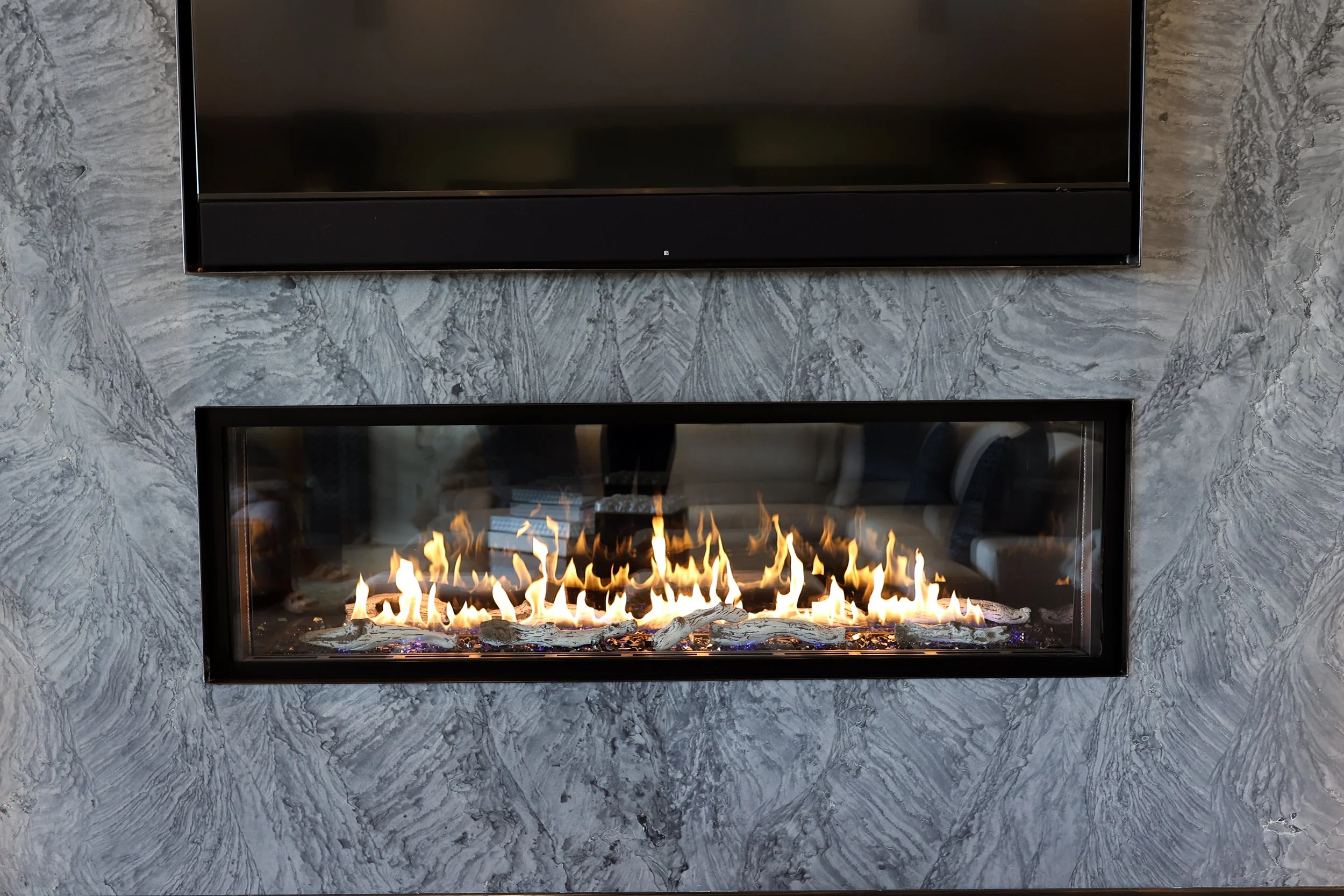 A modern gas fireplace with flames, set into a wall with gray marble tiles.
