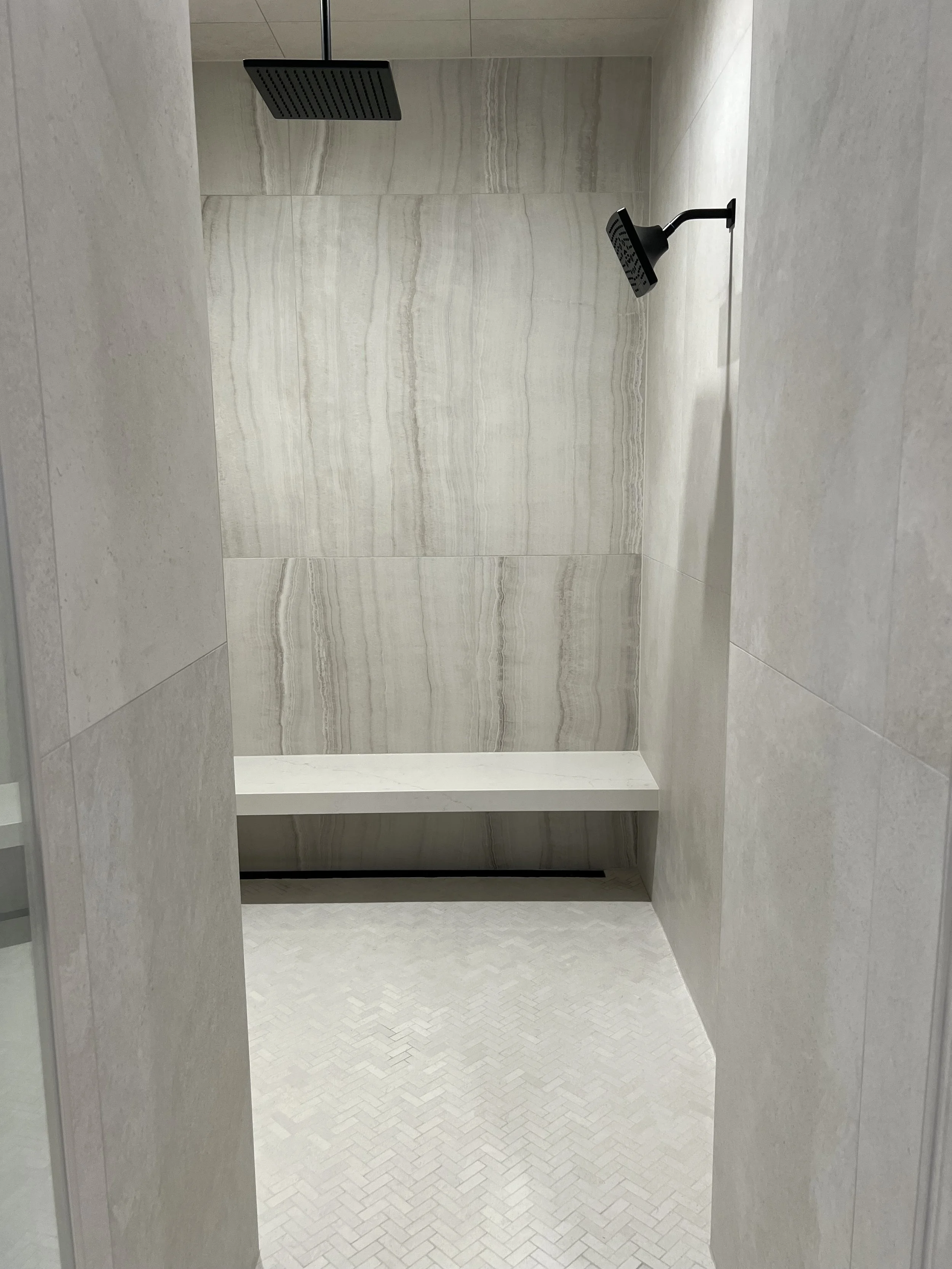 Interior of a modern shower with beige tiled walls, a ceiling-mounted rainfall showerhead, and a built-in bench.