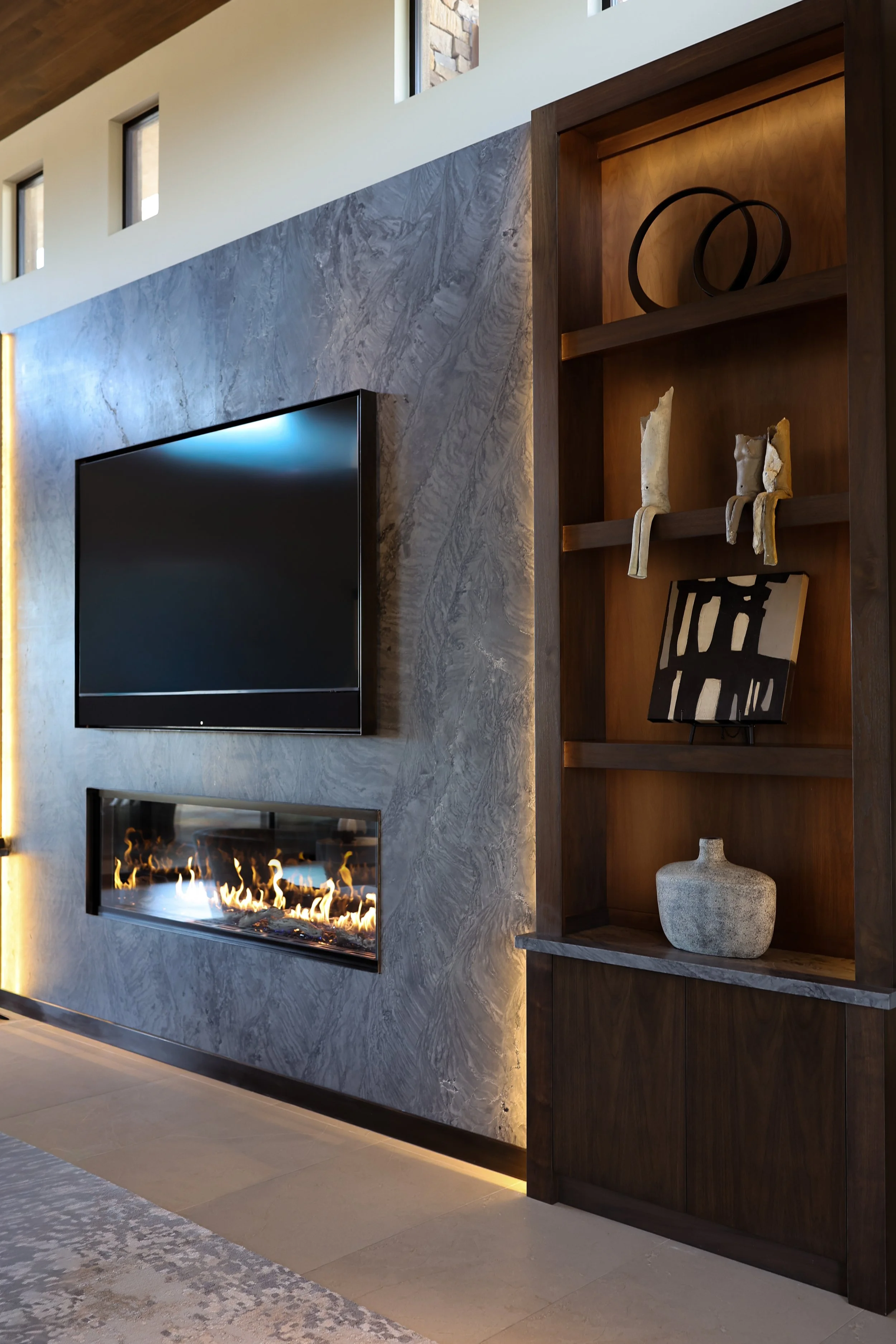 Modern living room with a wall-mounted flat-screen TV, a fireplace, and a wooden shelving unit with decorative items.