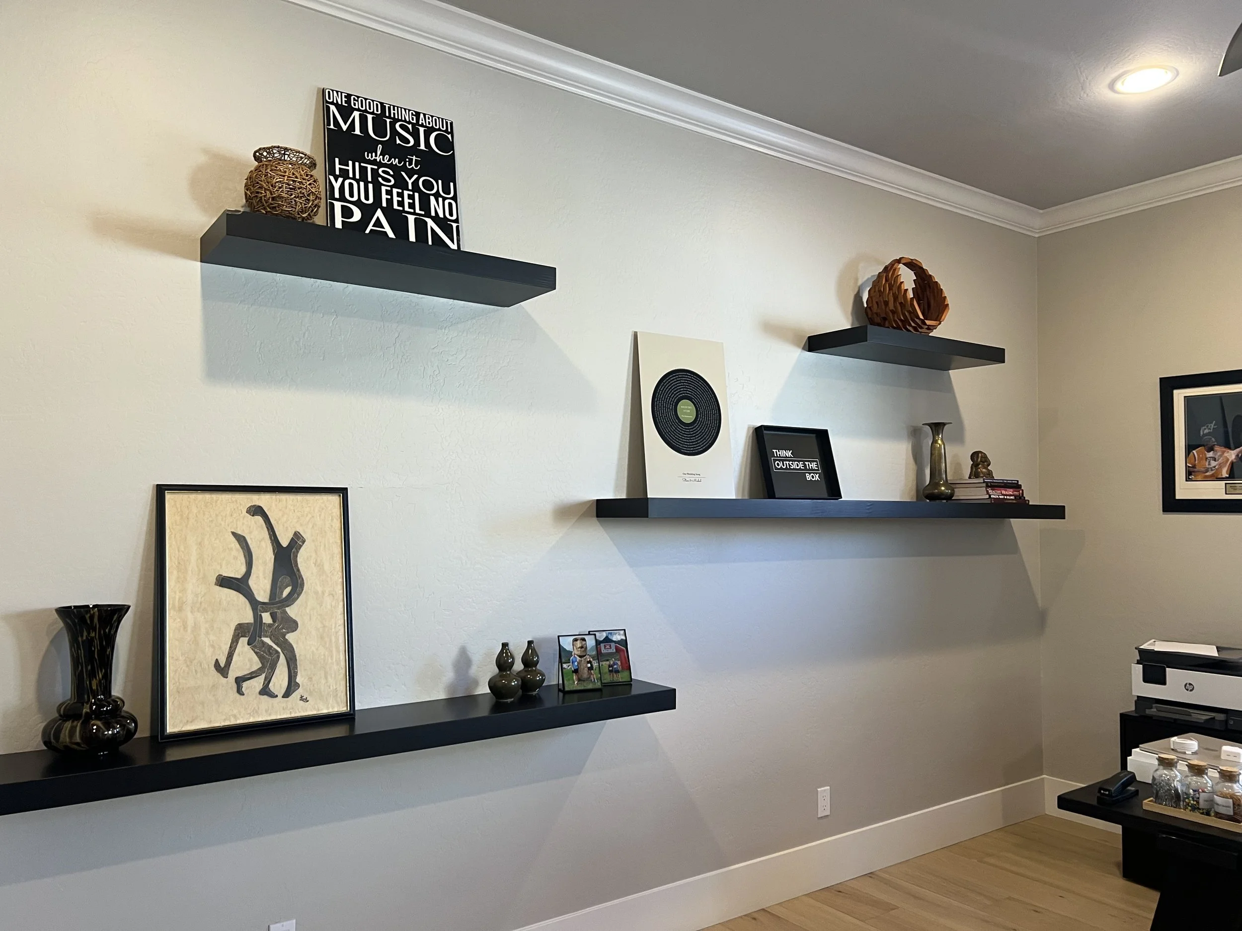Living room wall with two floating black shelves holding home decor items, framed art, and photos.