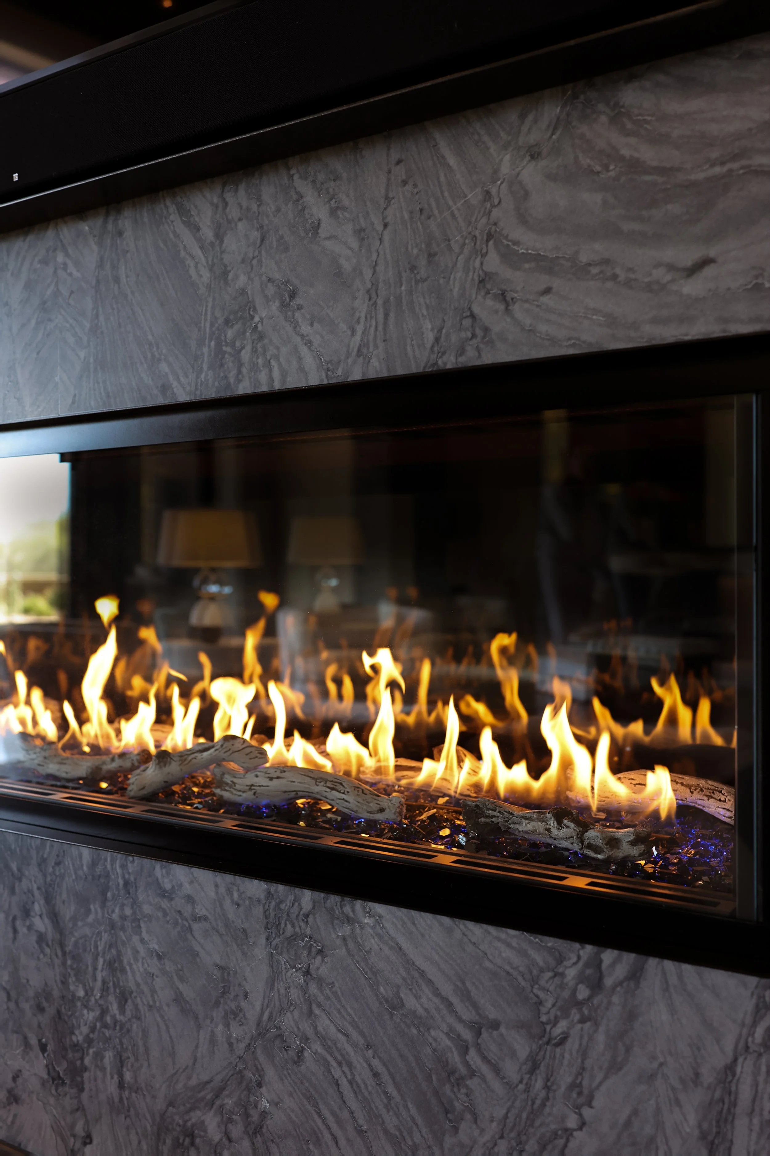 Modern fireplace with visible flames, set against a gray marble wall, with a black frame and glass front.