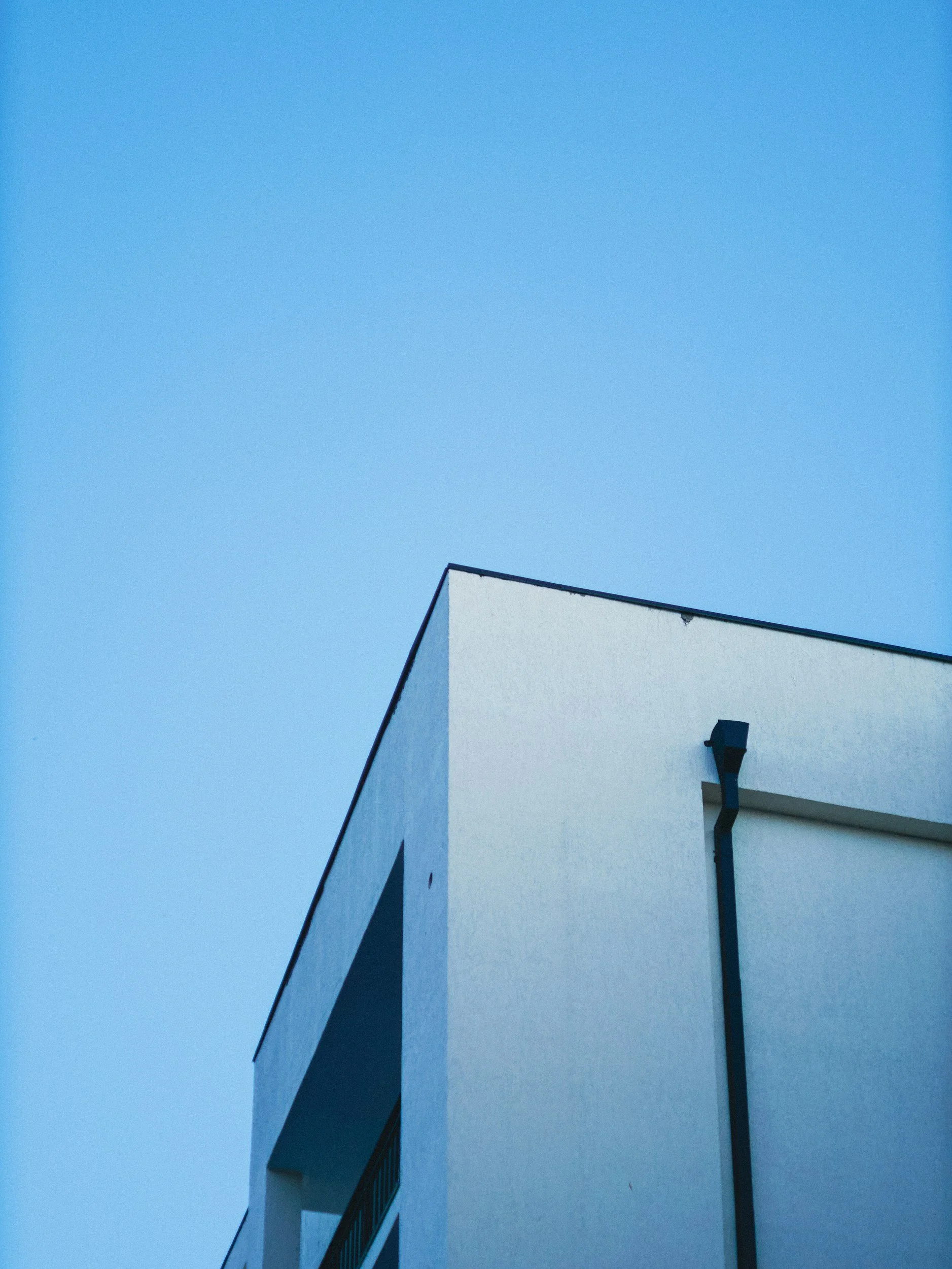 A white building with a flat roof and a black gutter against a clear blue sky.