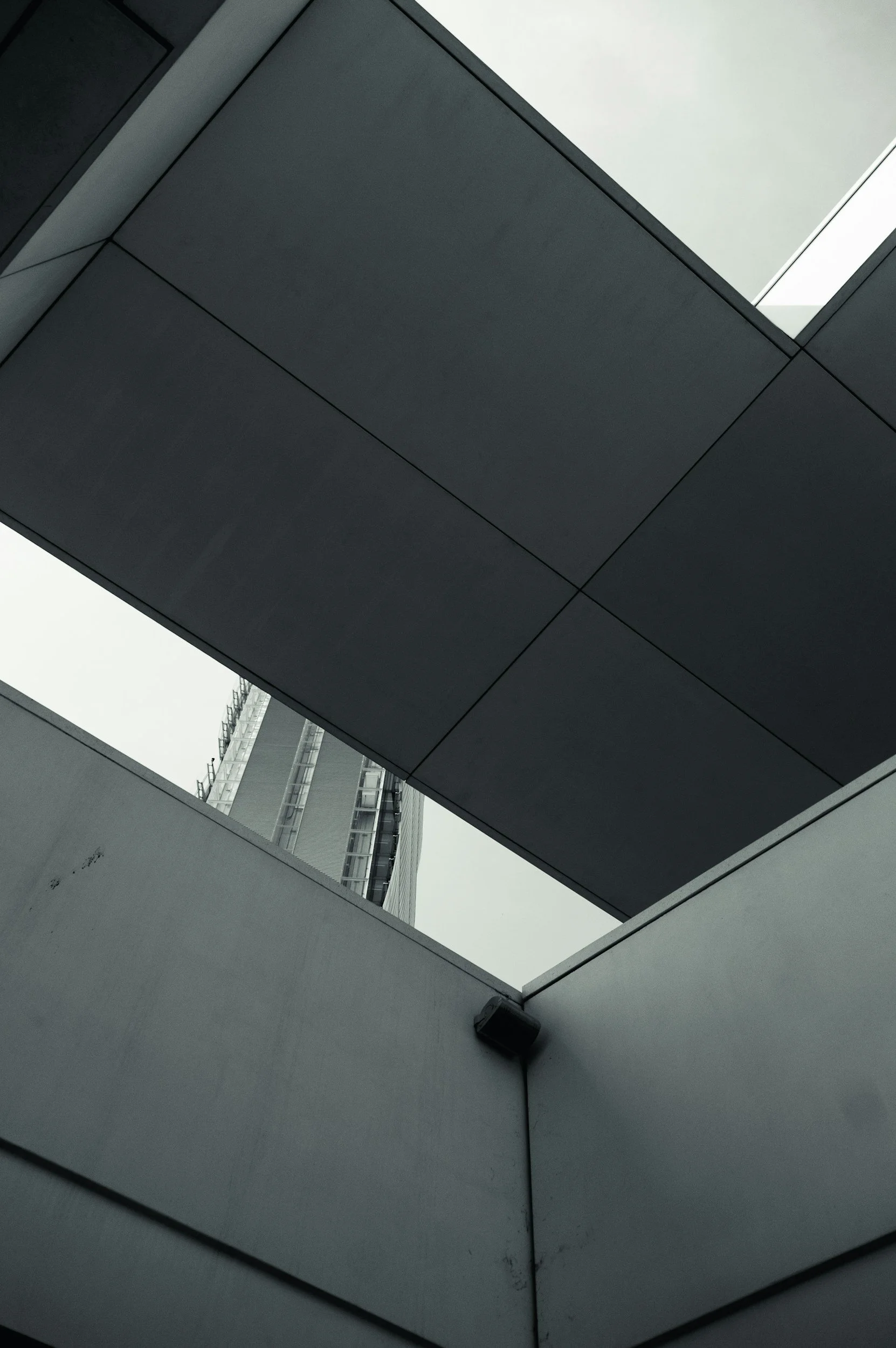 View looking up at modern building with glass and concrete surfaces, showing geometric shapes and architectural details.