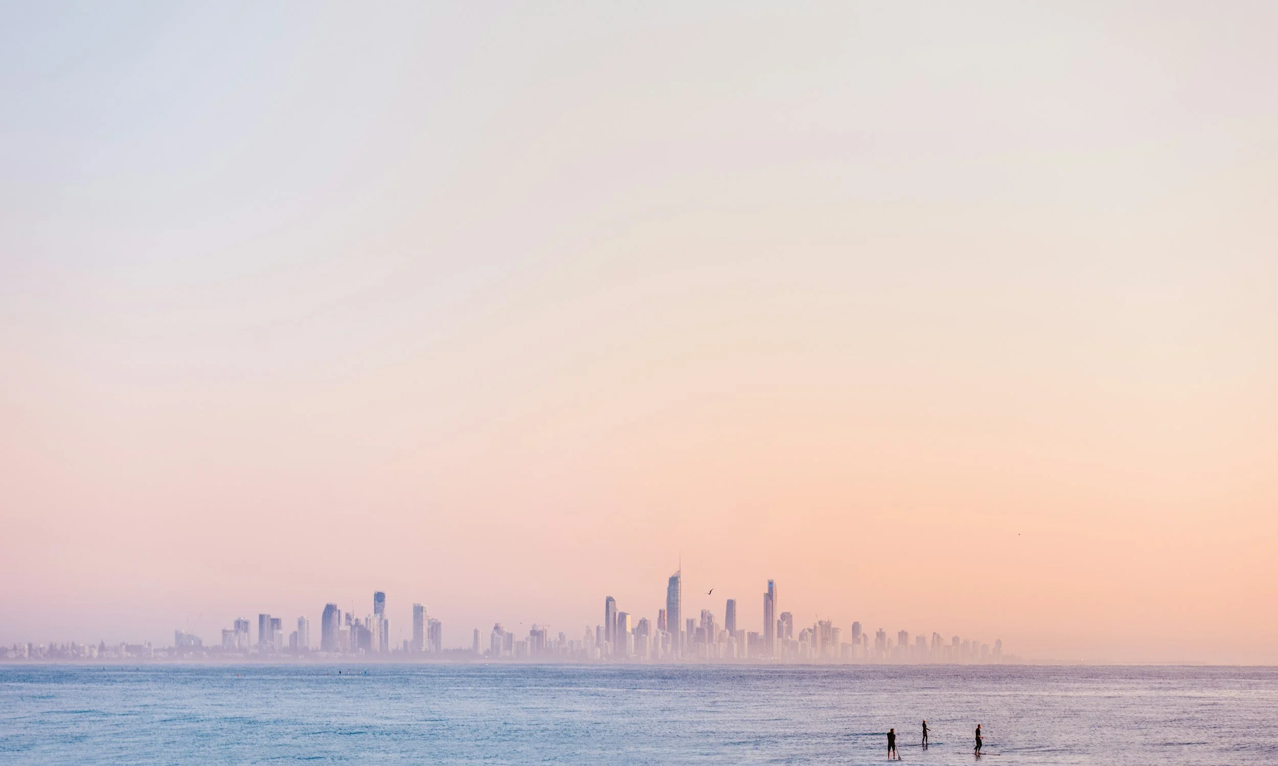 City skyline near the water at sunset with three people standing at the shore.