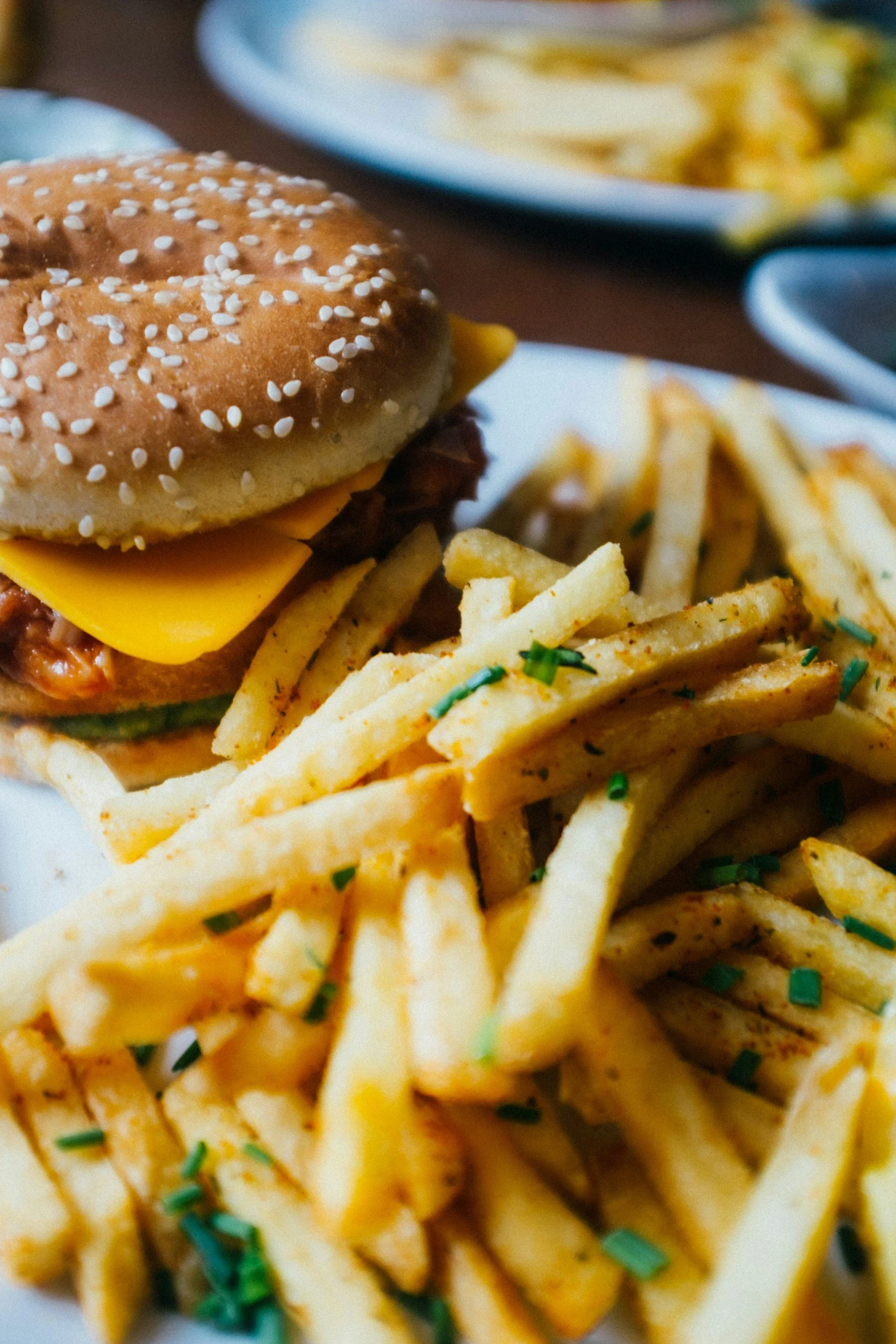 A cheeseburger with a sesame seed bun, cheese, beef patty, and toppings. Served with seasoned French fries garnished with chopped green herbs.