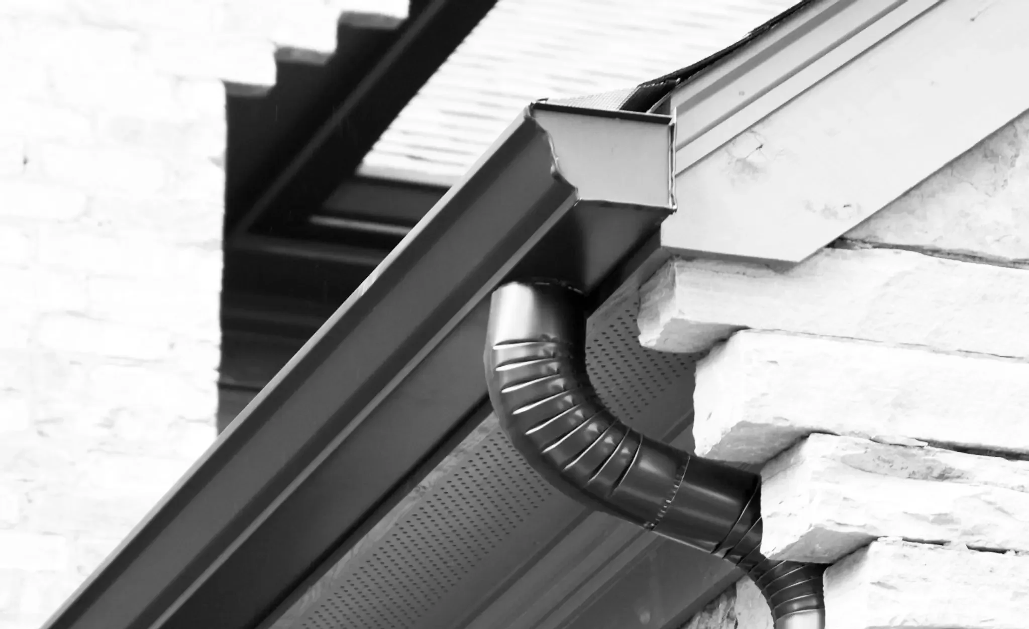 Close-up of house gutter system with downspout attached to the roof edge and wall, in black and white