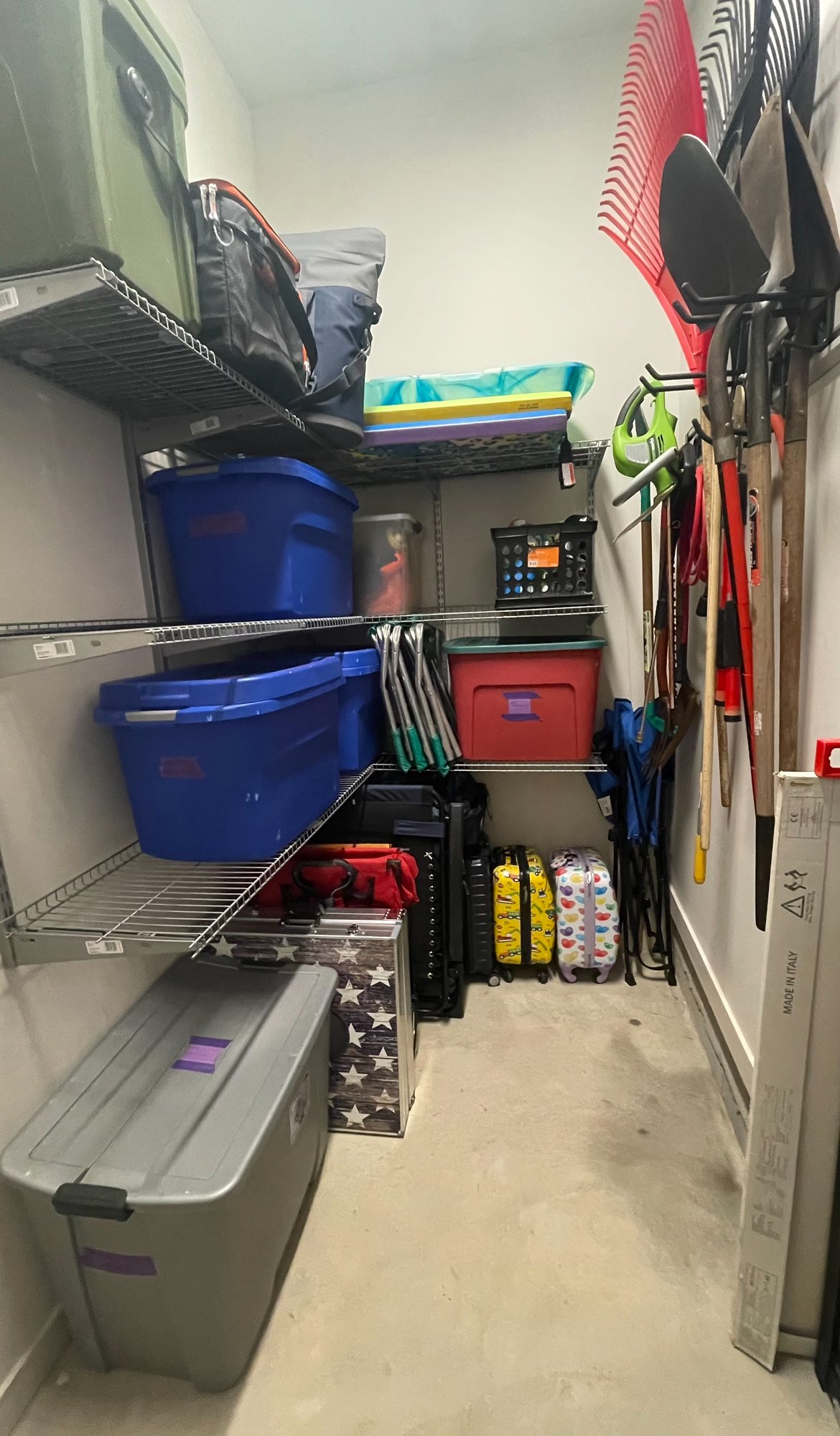The after picture of a storage room with blue bins, gray container, luggage, gardening tools, and sports equipment. Highly organized and efficient for client's ease.