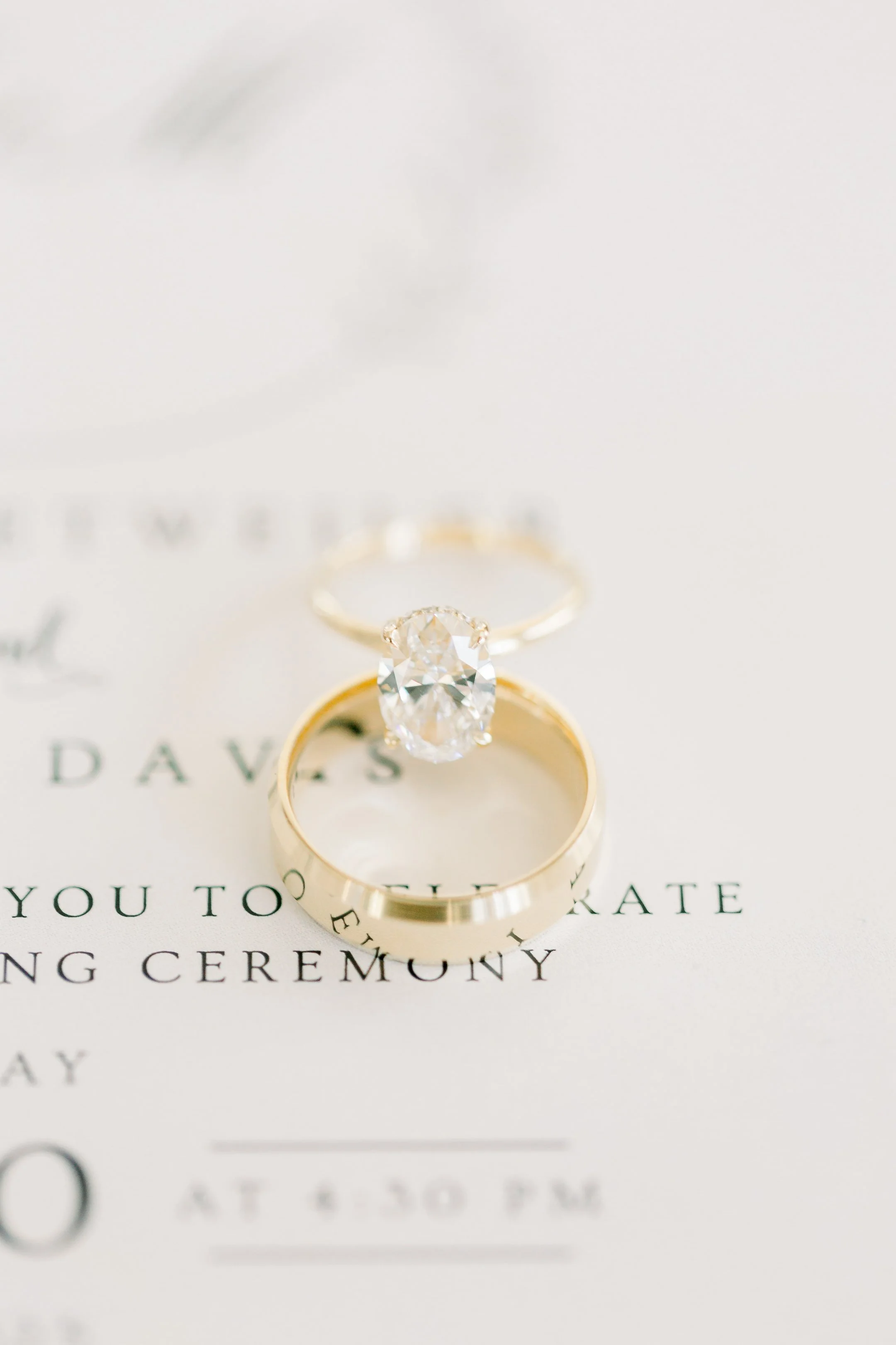 Close-up of a diamond engagement ring and a wedding band resting on a wedding invitation.