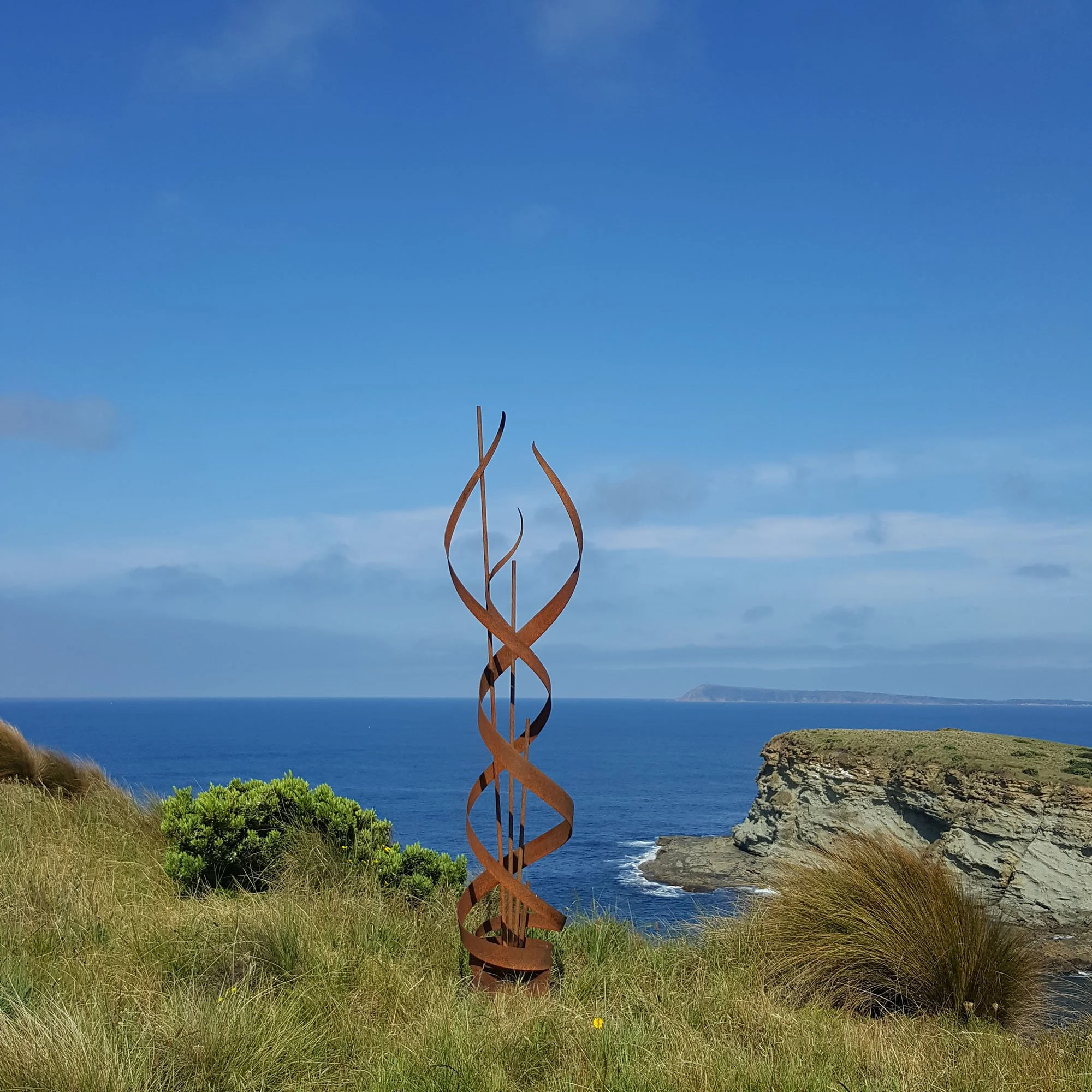 a sculpture representing flames rising up, located on a grassy clifftop looking out towards the ocean