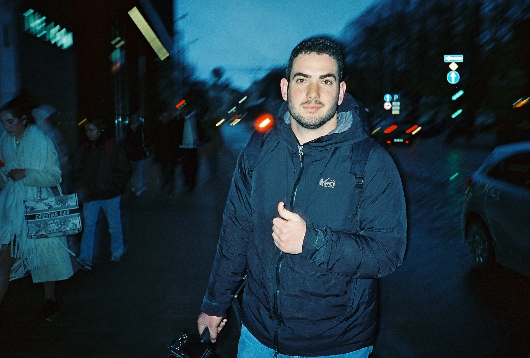 a young man holding a camera gives a thumbs up