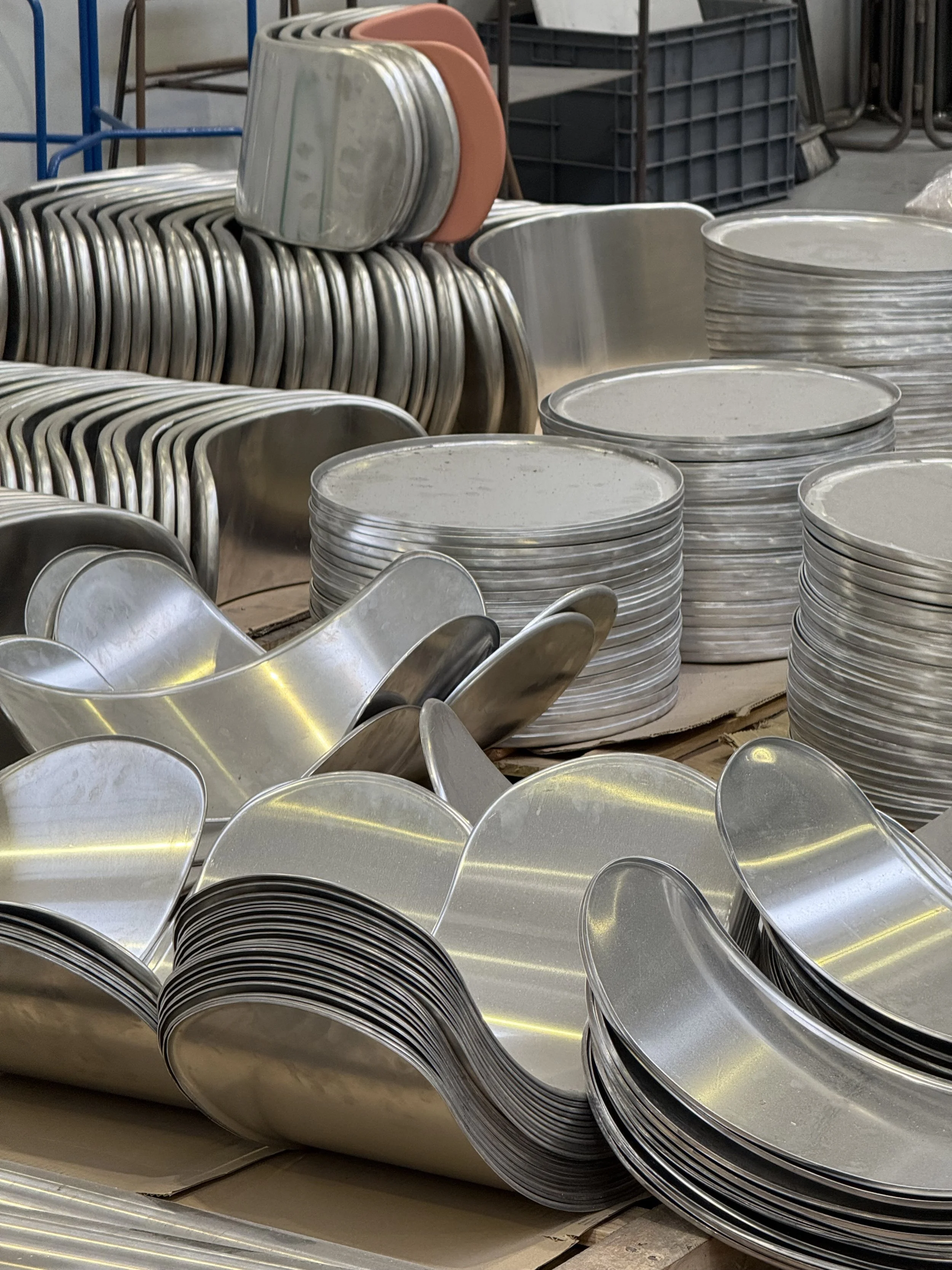 Stacks de pièces de vaisselle en métal, y compris des assiettes, des bols et des cuillères en métal, dans un environnement industriel ou de stockage.