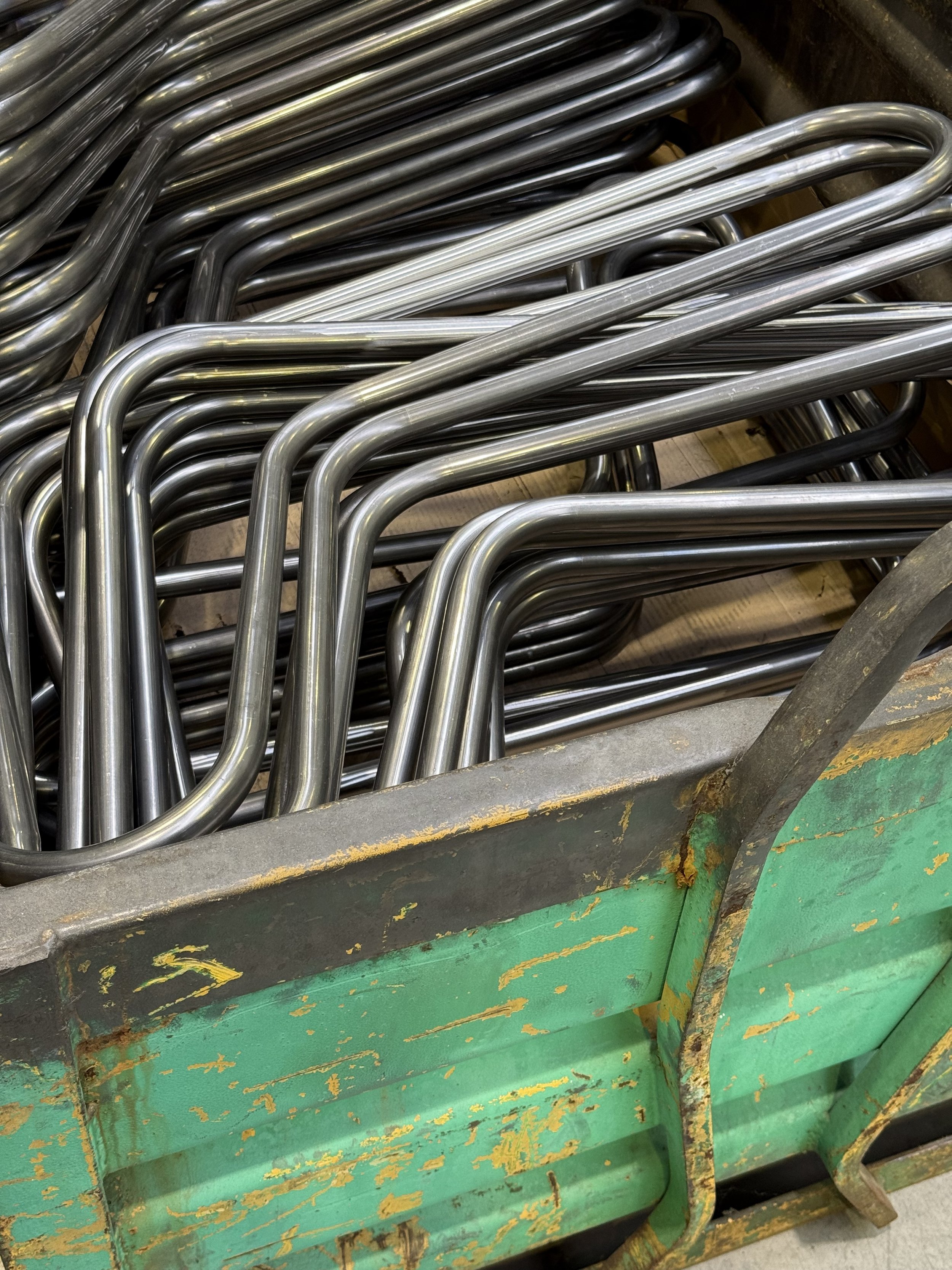 Un chariot rempli de barres métalliques en forme de U, de différentes couleurs argentée et sombre, dans un environnement industriel.