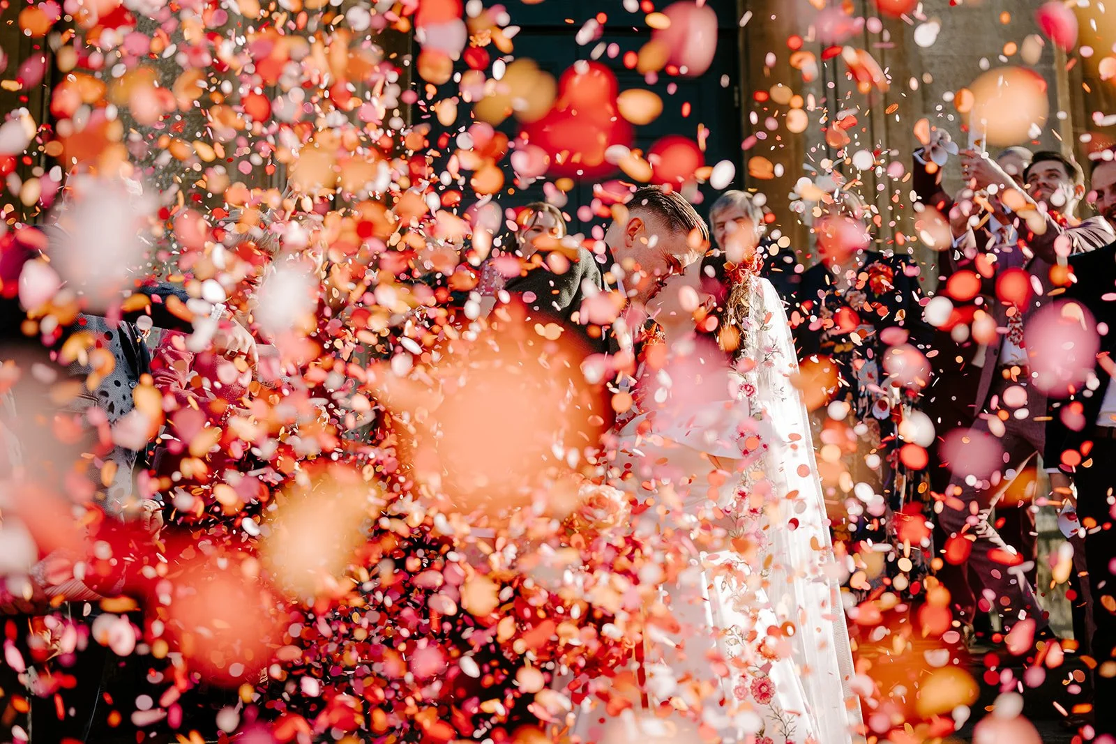 A bride and groom in a shower of colourful flutter darlings confetti at their October wedding golden hour