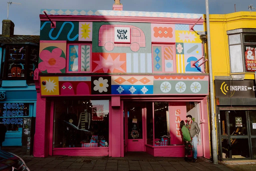A couple stand in front of a lucy and yak store in Brighton, wearing lucy and yak on their wedding day