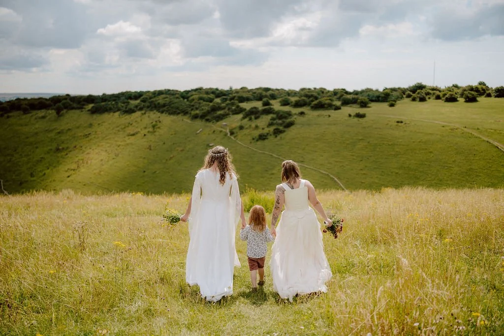 two brides and their kid walk hand in hand at devils dyke