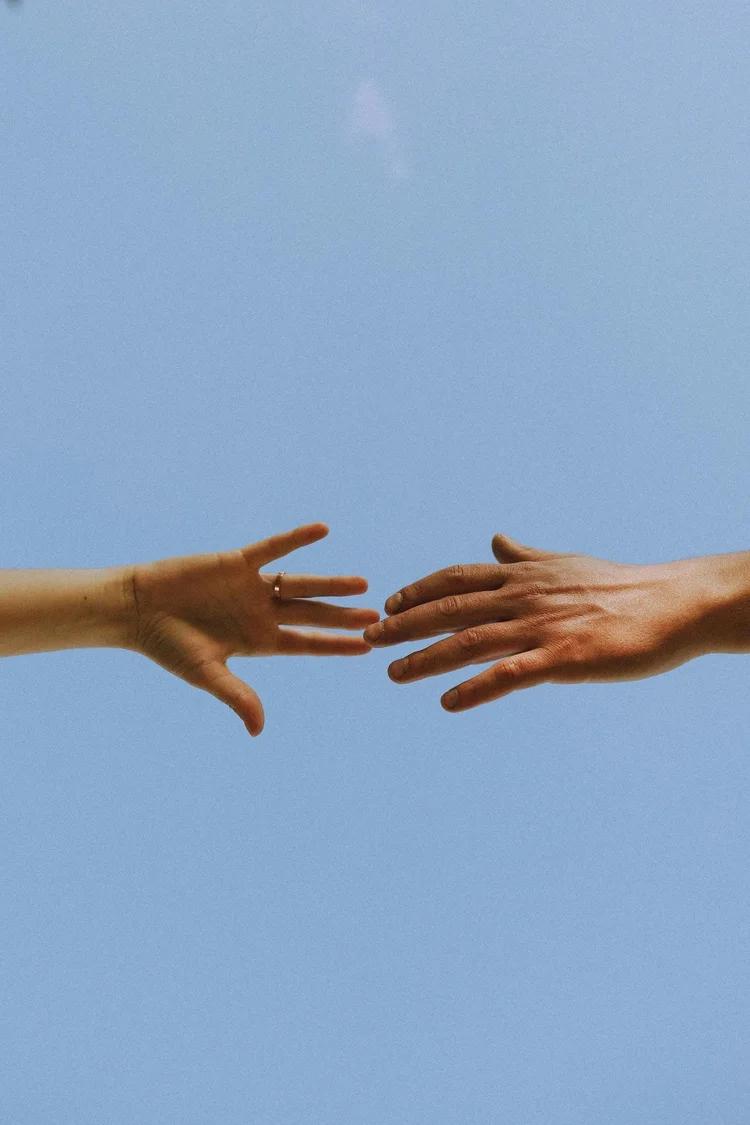 Two hands reaching toward each other against a blue sky