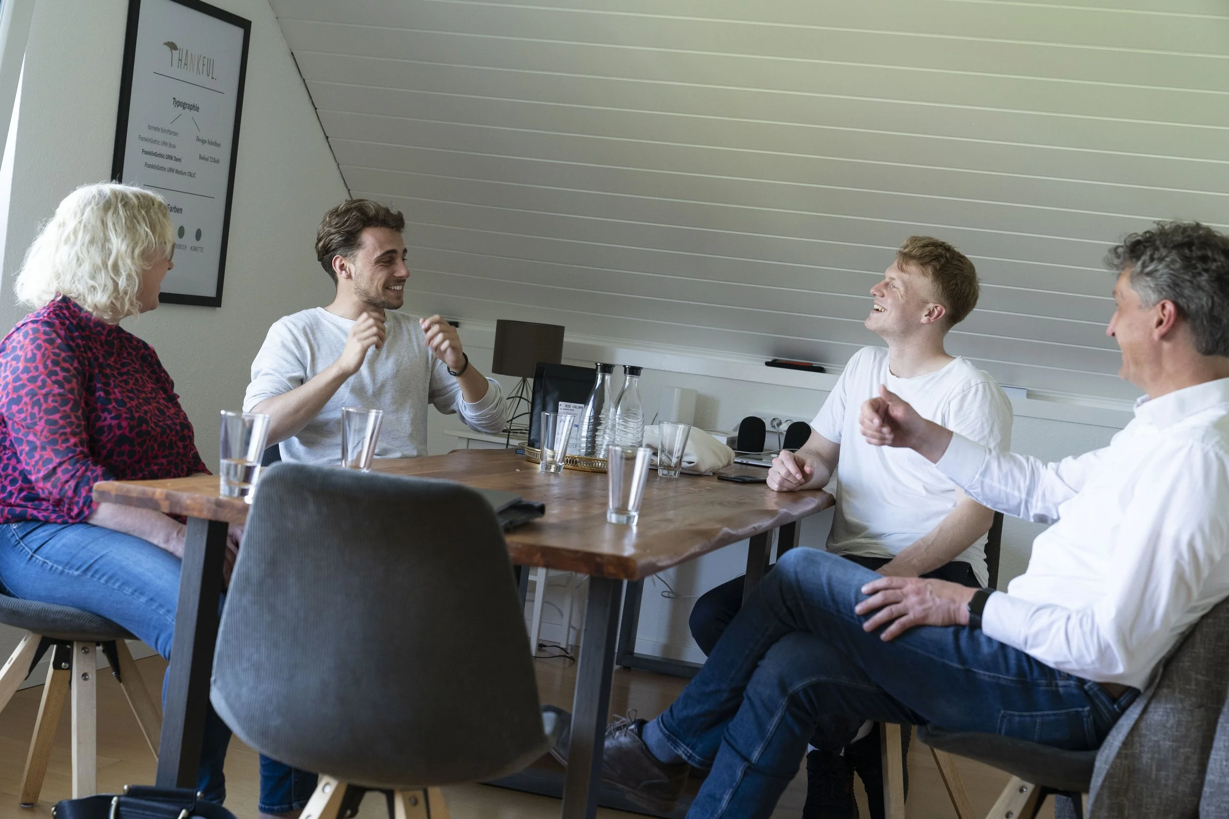 Fünf Menschen sitzen bei einem Treffen im Conference Room und lachen.