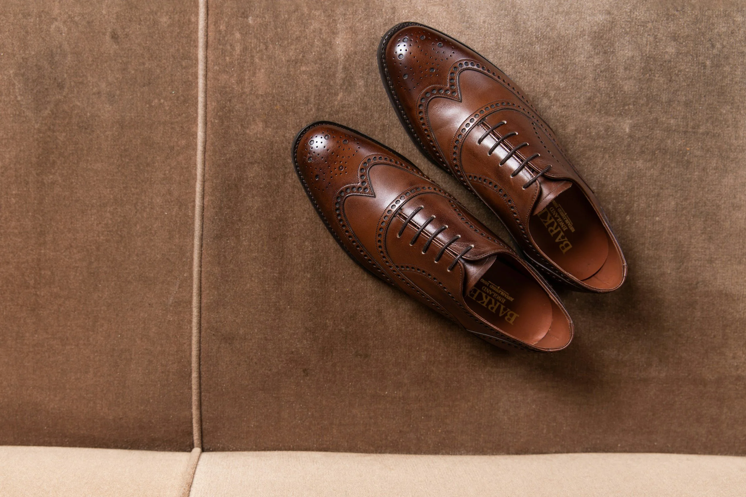 Pair of brown leather dress shoes on a tiled floor.
