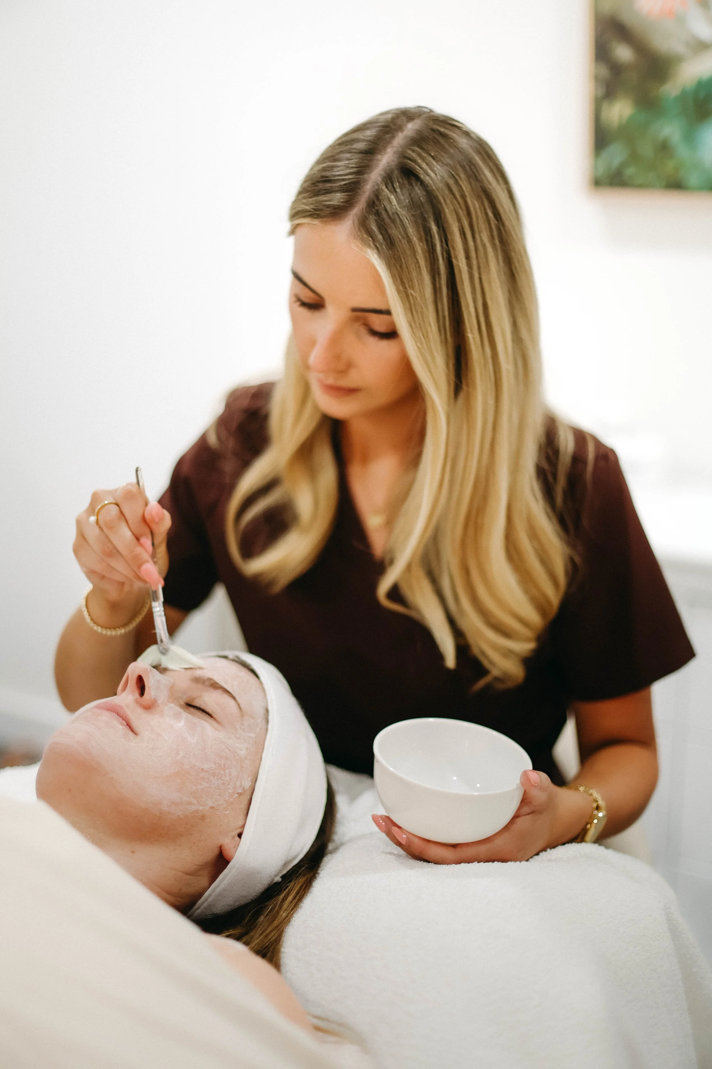 A woman receiving a facial treatment from an esthetician in a spa setting
