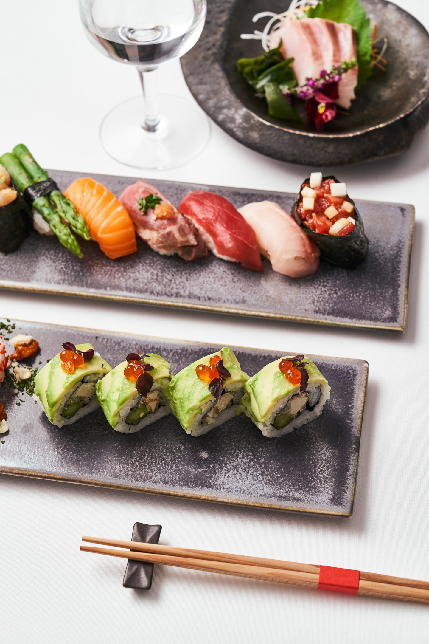 Assorted sushi rolls on black plates with a glass of red wine.