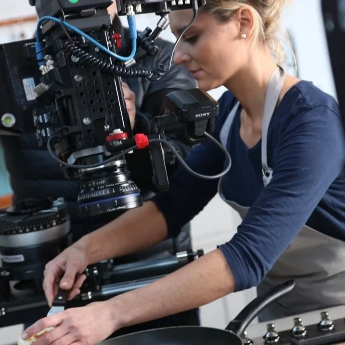 A woman operating a professional camera on a tripod in a studio or production setting.