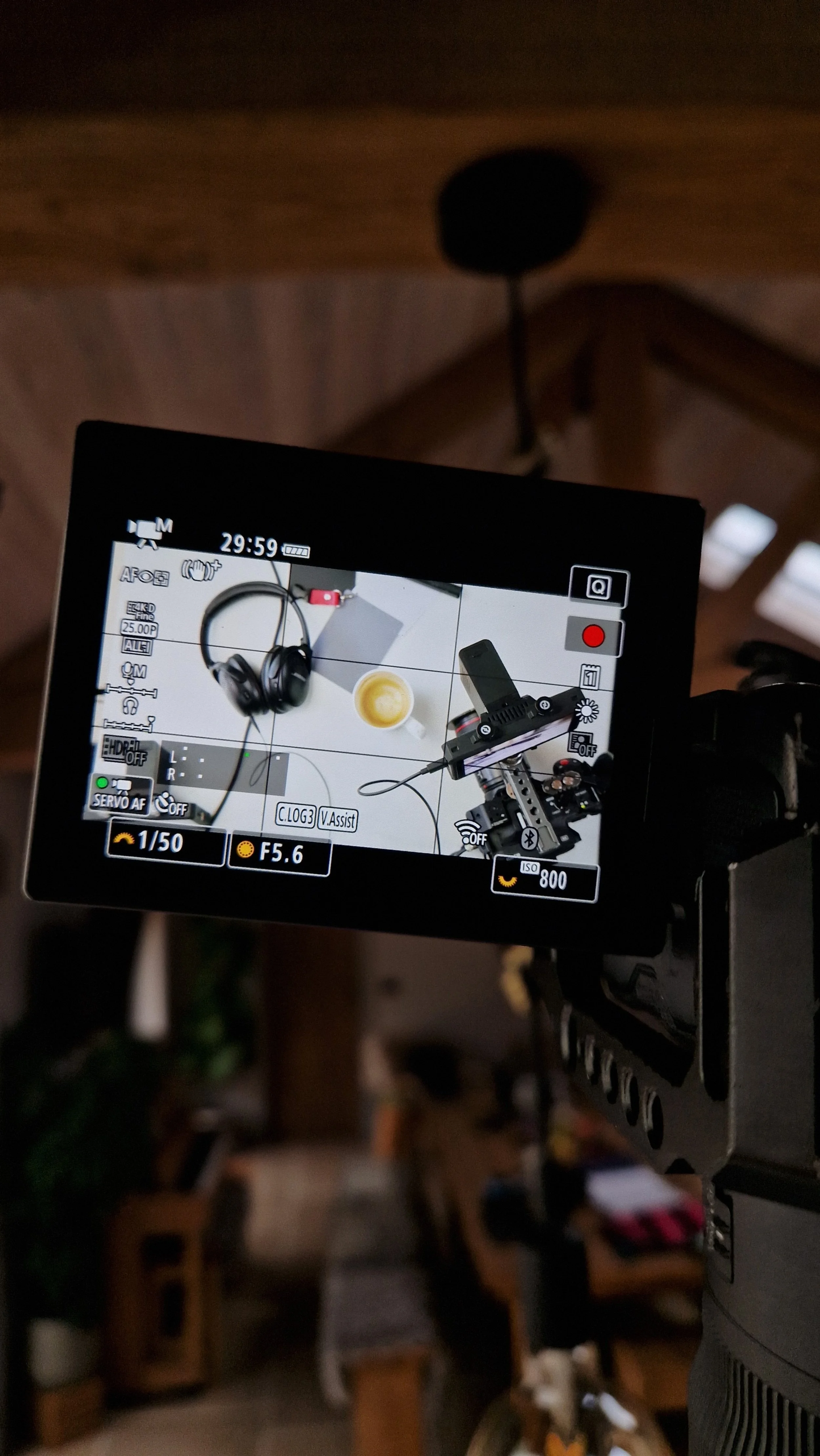 View of camera's LCD screen showing a pair of headphones, a cup of coffee, and camera accessories on a white surface, with photo settings displayed.